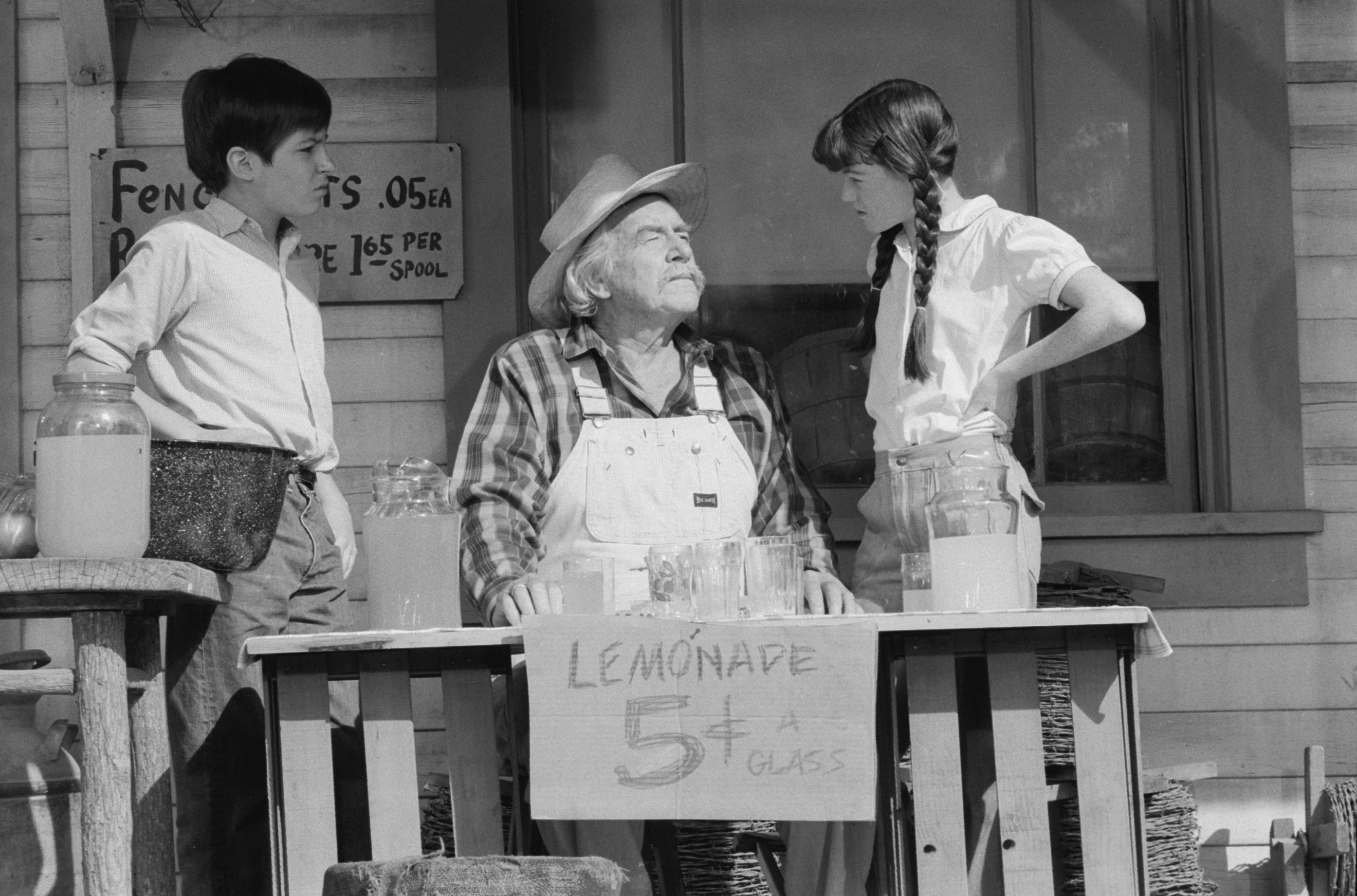 Will Geer as Zeb Walton sitting behind a lemonade stand as fellow co-star child actors David Harper as Jim-Bob Walton and Kami Cotler as Elizabeth Walton listen during a scene on "The Waltons" entitled "The Revelation," aired on January 13, 1978. / Source: Getty Images
