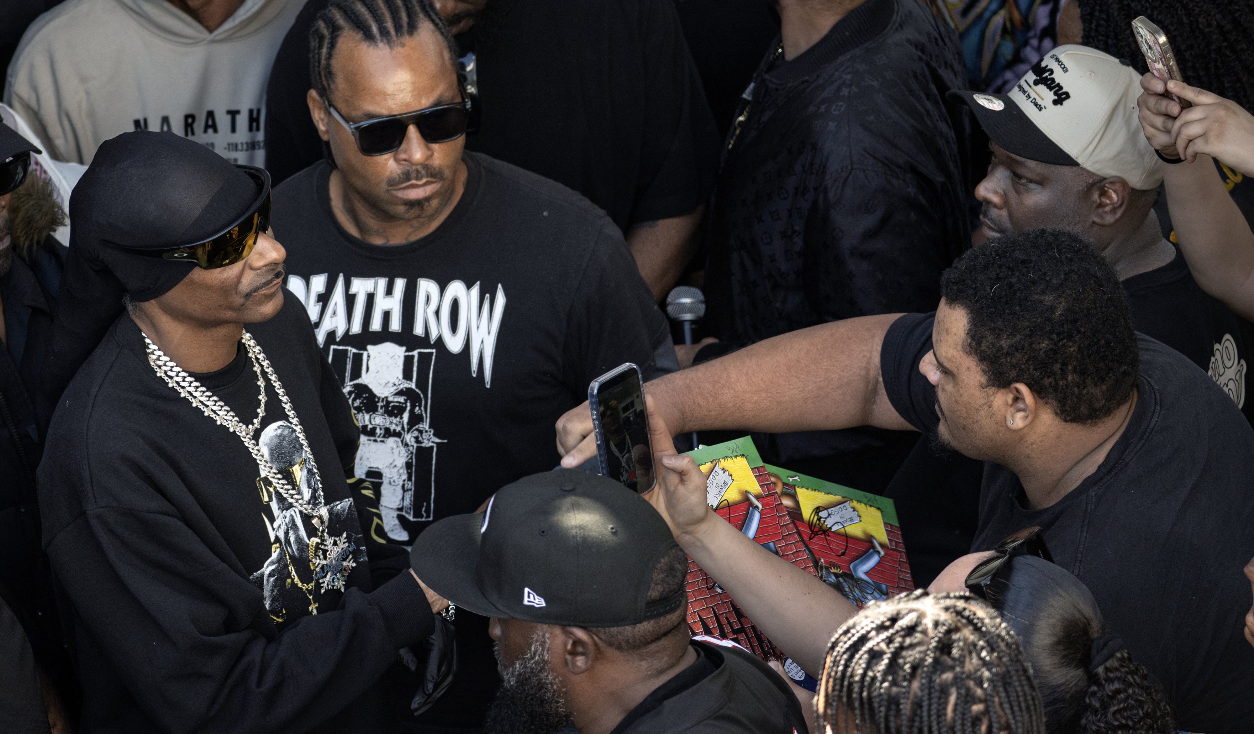 Snoop Dogg, far left, takes time to sign an autograph as he makes his way through the crowd for the ribbon-cutting ceremony | Source: Getty Images