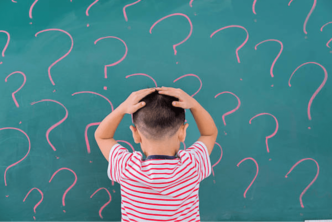 Little boys stand's, facing a green chalkboard with question marks written on it | Source: Getty Images