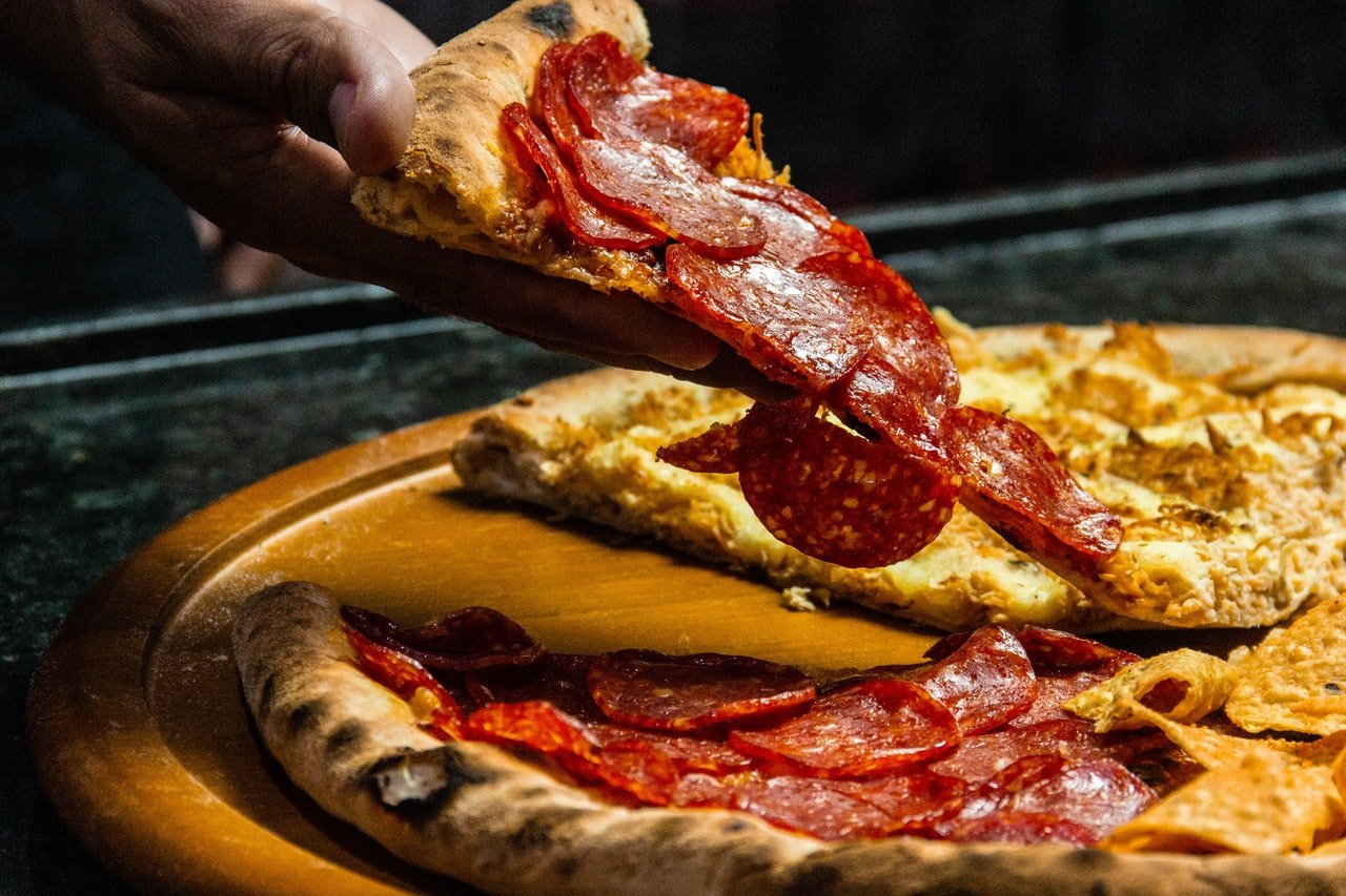 Photo of a hand holding a slice of pizza | Photo: Pexels