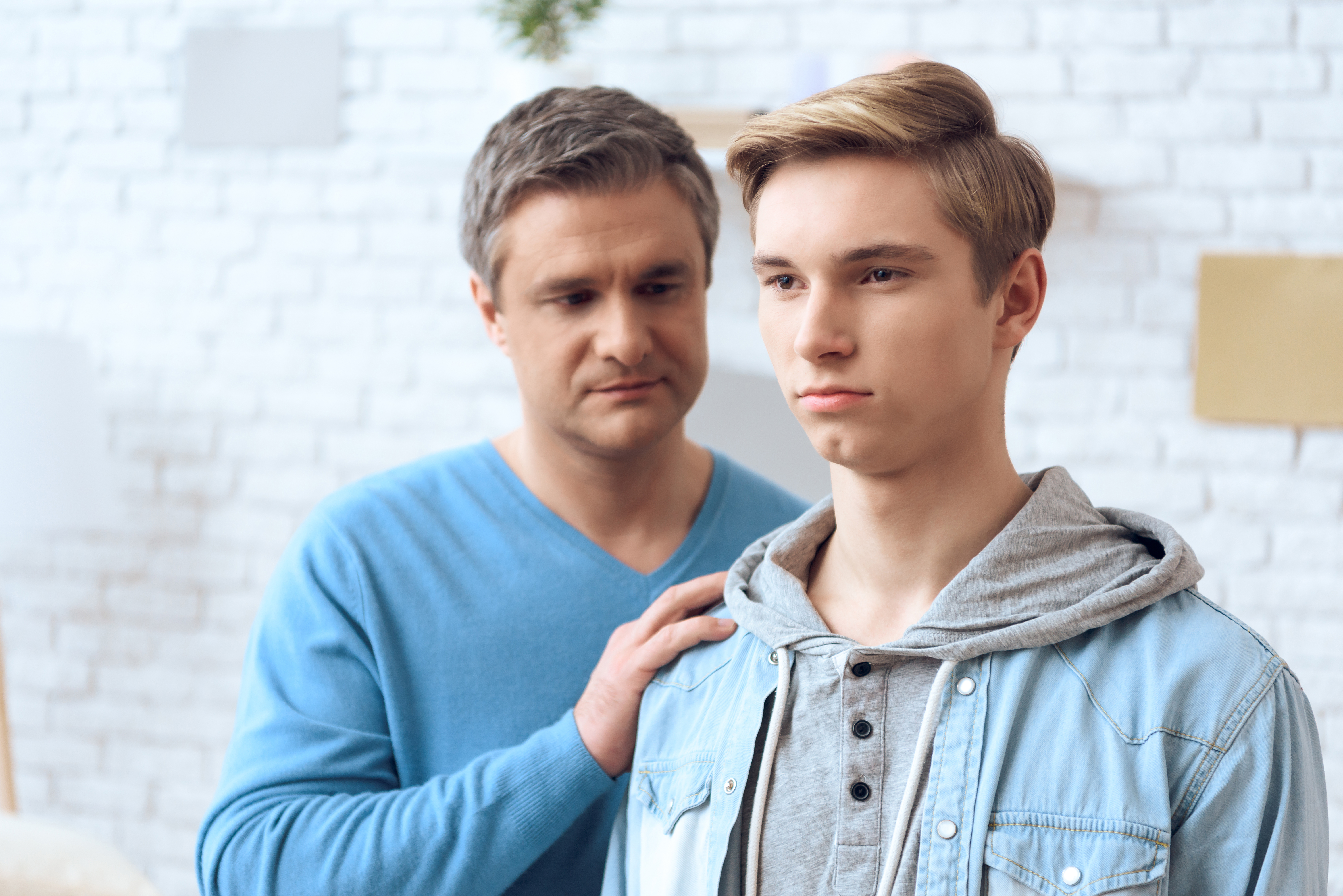 Boy staring into the distance as his father touches his shoulder. | Source: Shutterstock