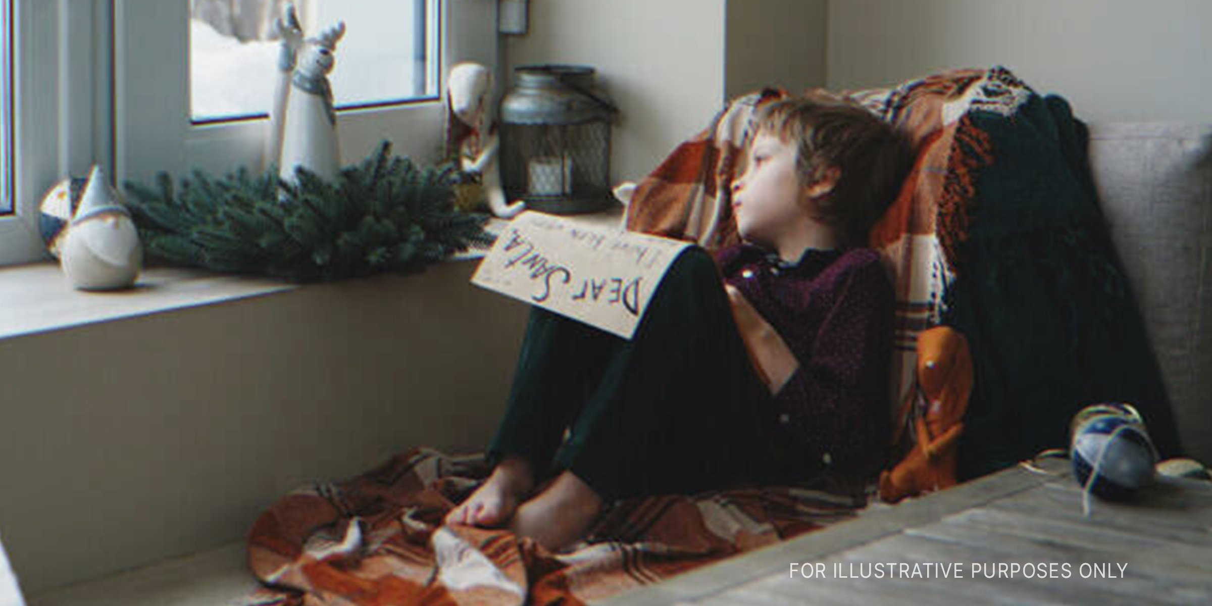 Boy holds letter to Santa while looking out window | Source: Getty Images