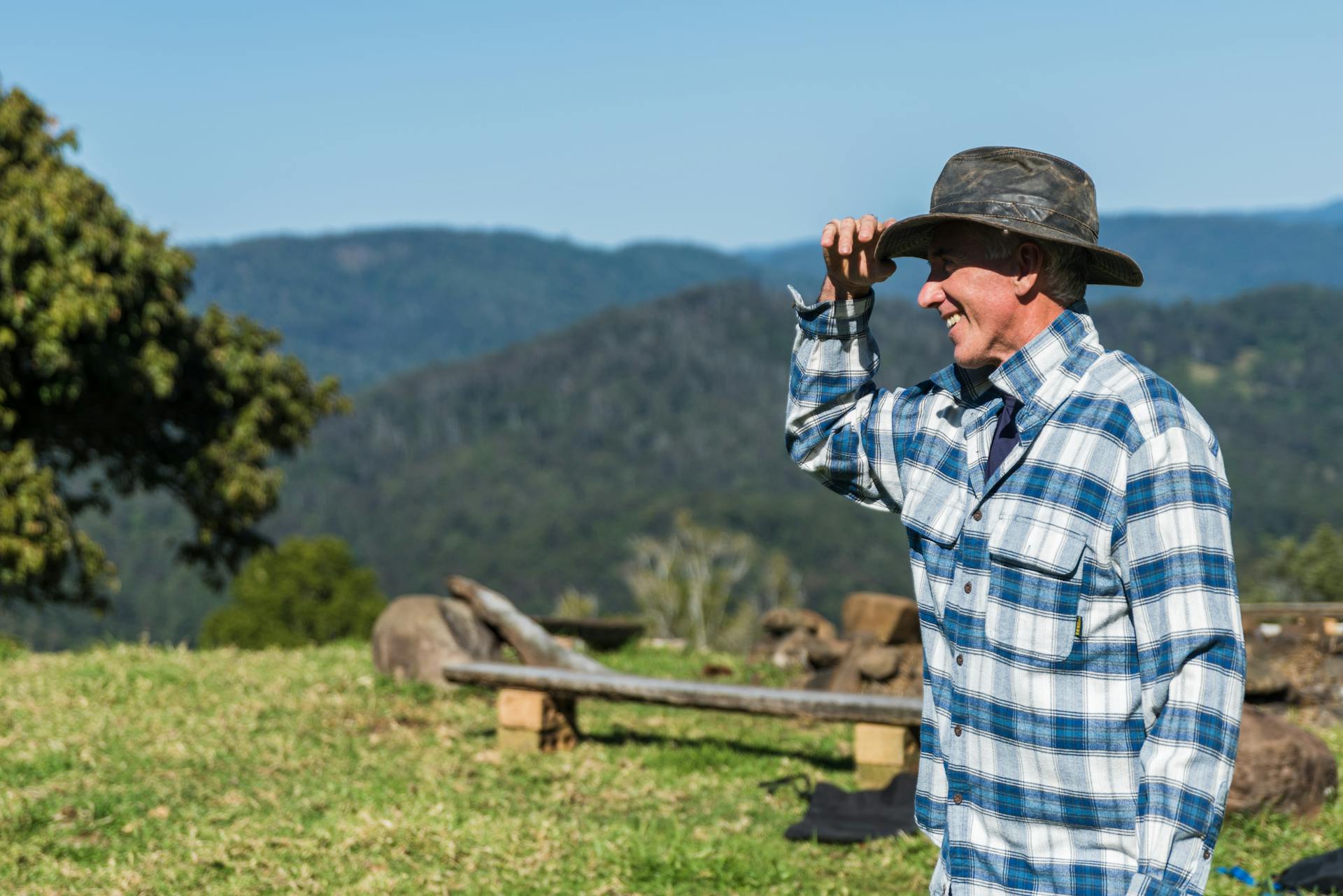 A man wearing a blue and white checked shirt and a black hat standing on a farm | Source: Pexels