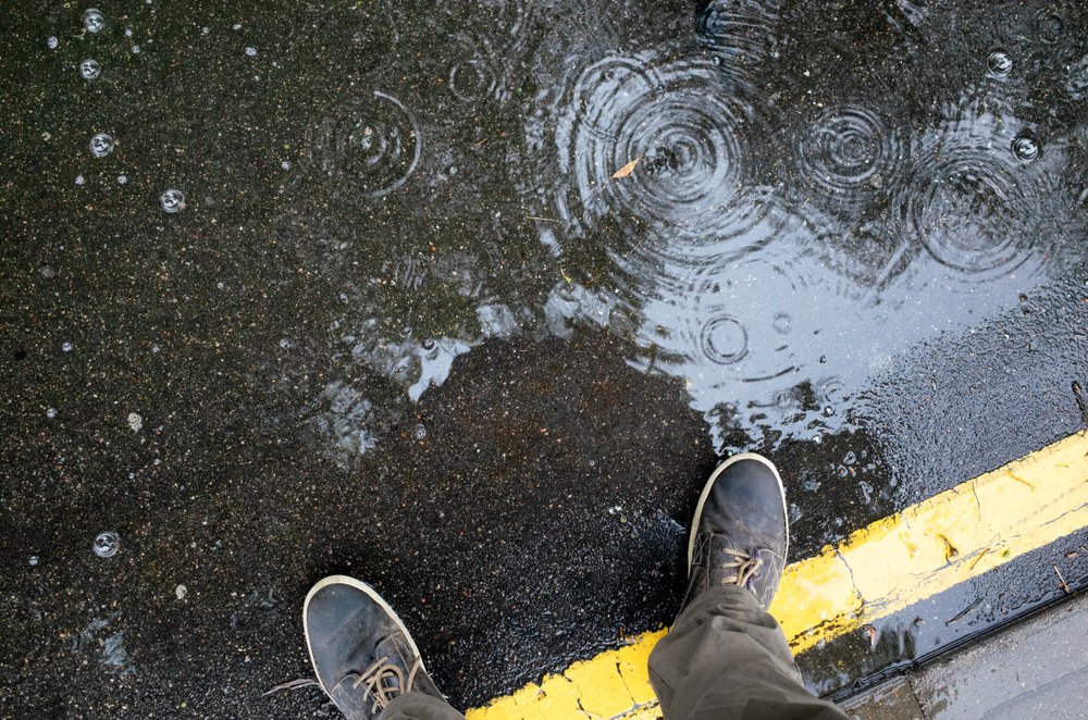 Man standing in rainwater puddle on a sidewalk | Photo: Shutterstock/IU Liquid and water photo