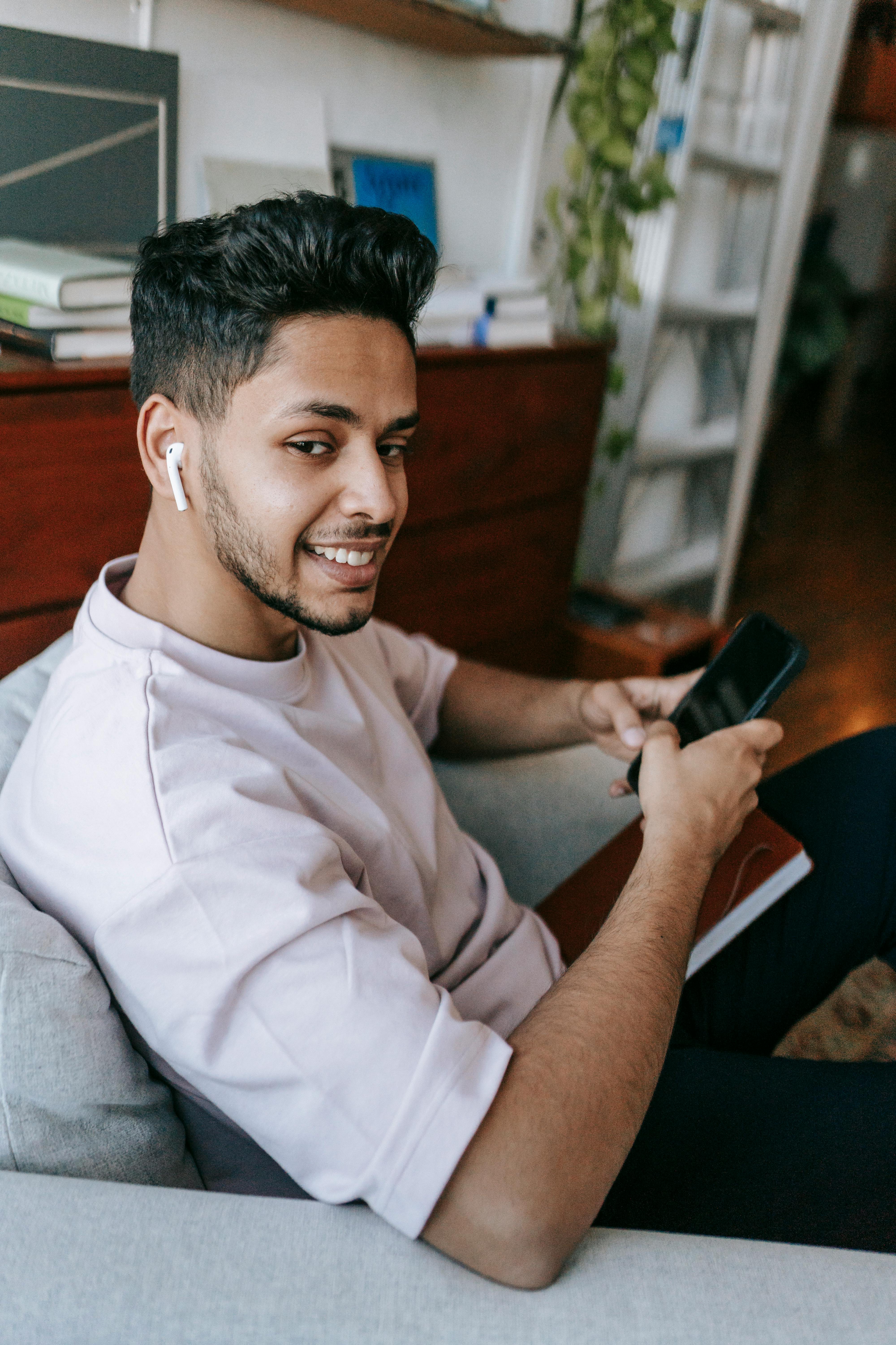 A happy man using his phone and ear pods | Source: Pexels