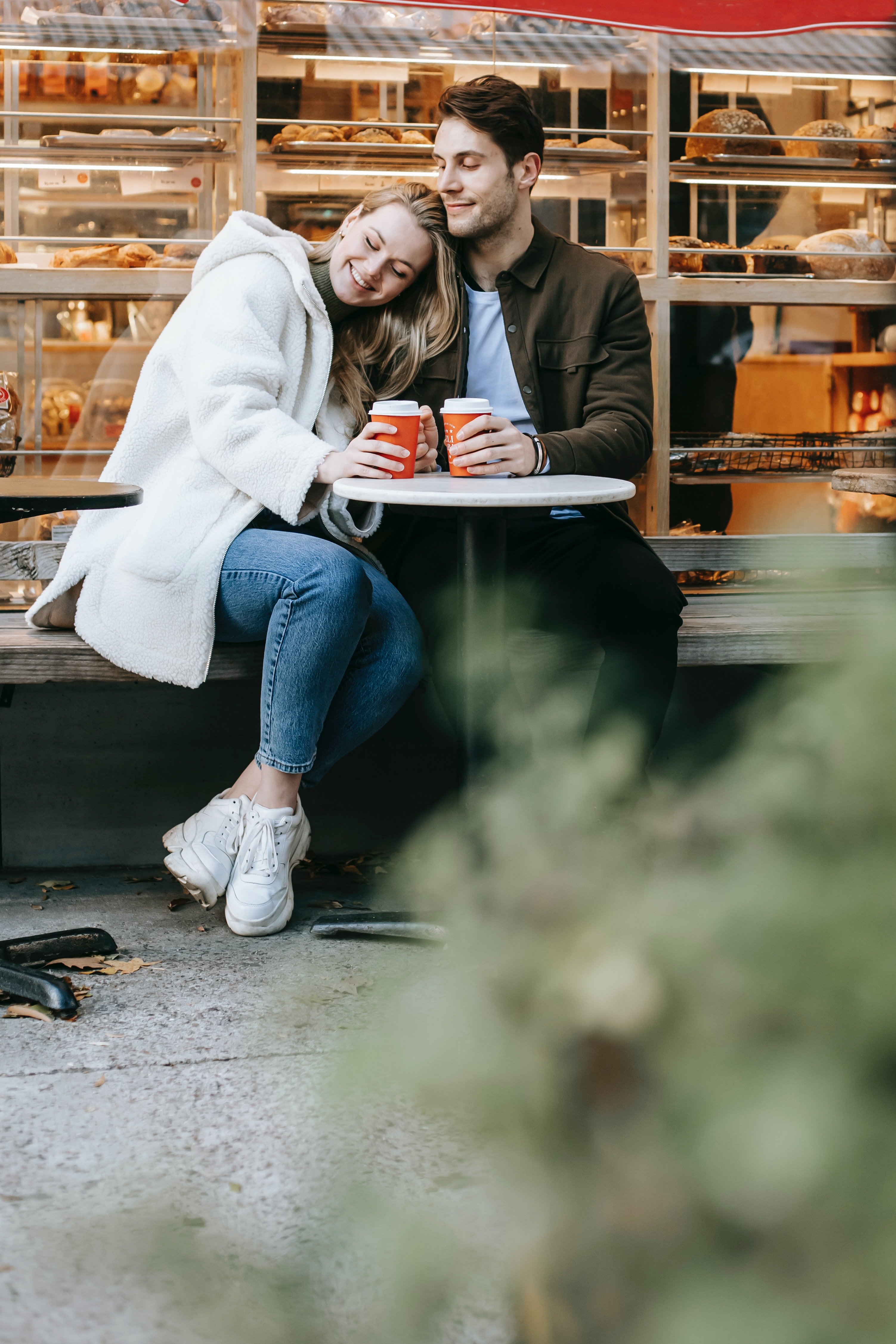 Pictured: A couple sitting at a street cafe with cups of drinks with the woman resting her head on her significant other | Source: Pexels 