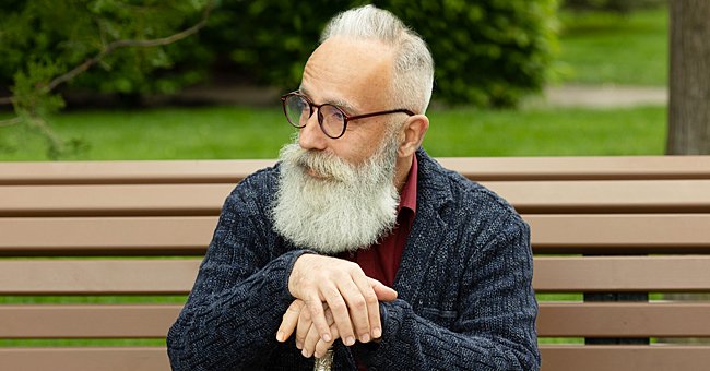 An old man rests on his cane while sitting on a bench | Photo: Shutterstock