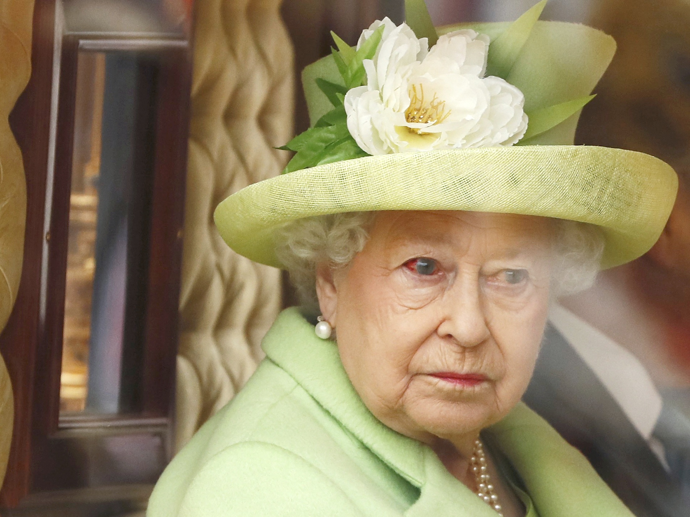 During the ceremonial welcome for Colombian President Santos, Queen Elizabeth II is captured riding in a horse-drawn carriage. Dressed in mint green with pearl accessories, the queen's bloodshot eye quietly contrasts with the day's formal pageantry.