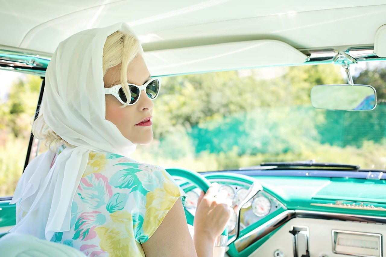 A woman wearing a headscarf and sunglasses as she looks outside her car passenger window | Photo: Pixabay/Jill Wellington