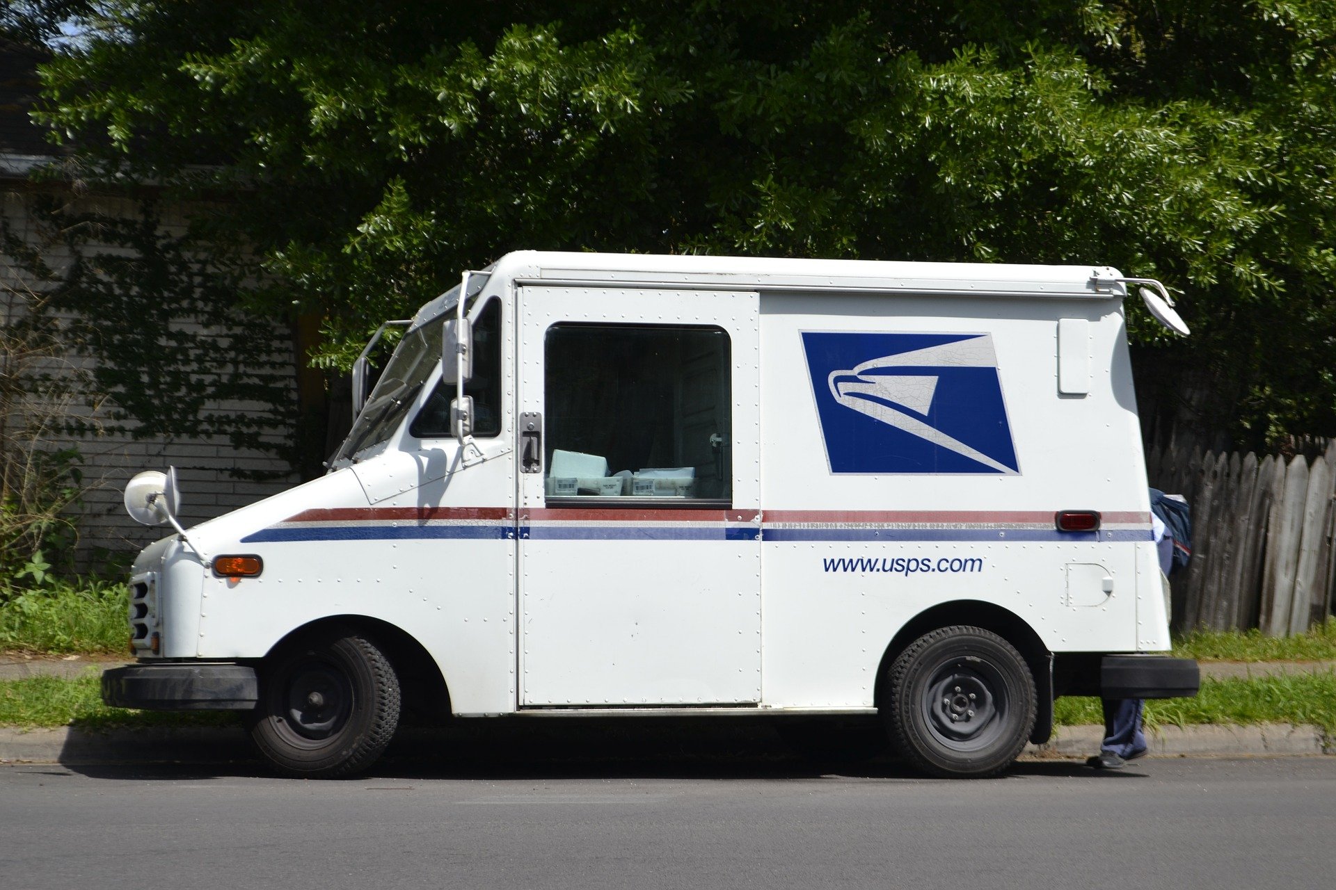 A mailman getting mail out of the back of his truck. | Source: Pixabay.