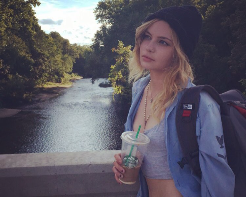 Daveigh Chase holds a Starbucks drink while standing on a bridge overlooking a river in a photo shared in August 2015, months before her online presence began to fade. | Source: Instagram/daveighc