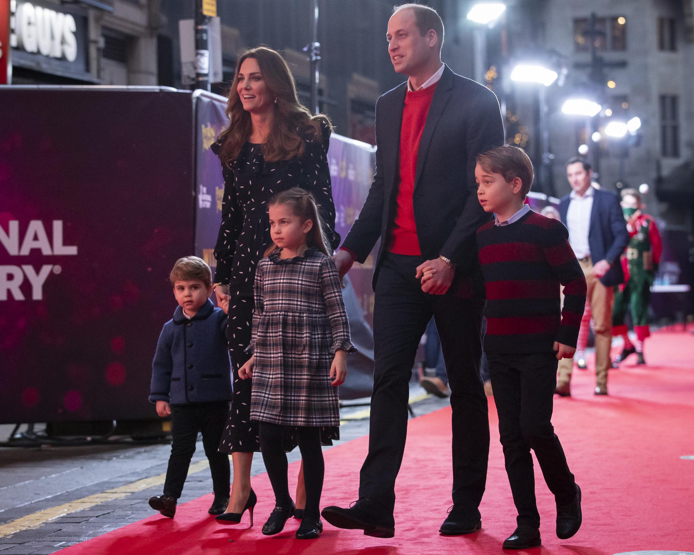 The Wales family walk a red carpet together at London's Palladium Theatre in December 2020 — William in a red jumper, Catherine in a printed dress, and Charlotte centre-stage in a grey tartan frock, flanked by her brothers.