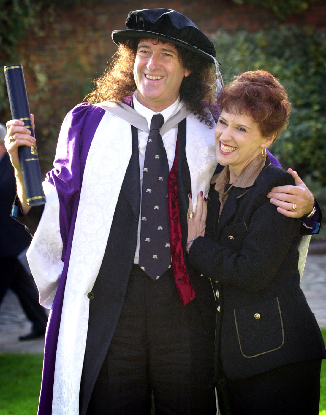 Brian May and Anita Dobson after he was awarded an honorary Doctorate of Science by the University of Hertfordshire, outside St Albans cathedral, on November 19, 2002. | Source: Getty Images