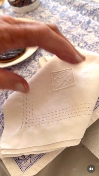 The embroidered napkin comes into sharp focus as Lady Pamela Hicks lifts it, revealing intricate stitching that holds deep personal significance. The close-up draws attention to the craftsmanship and sentiment behind the item, tying into her remark about finally using pieces saved from her wedding. | Source: Instagram/indiahicksstyle