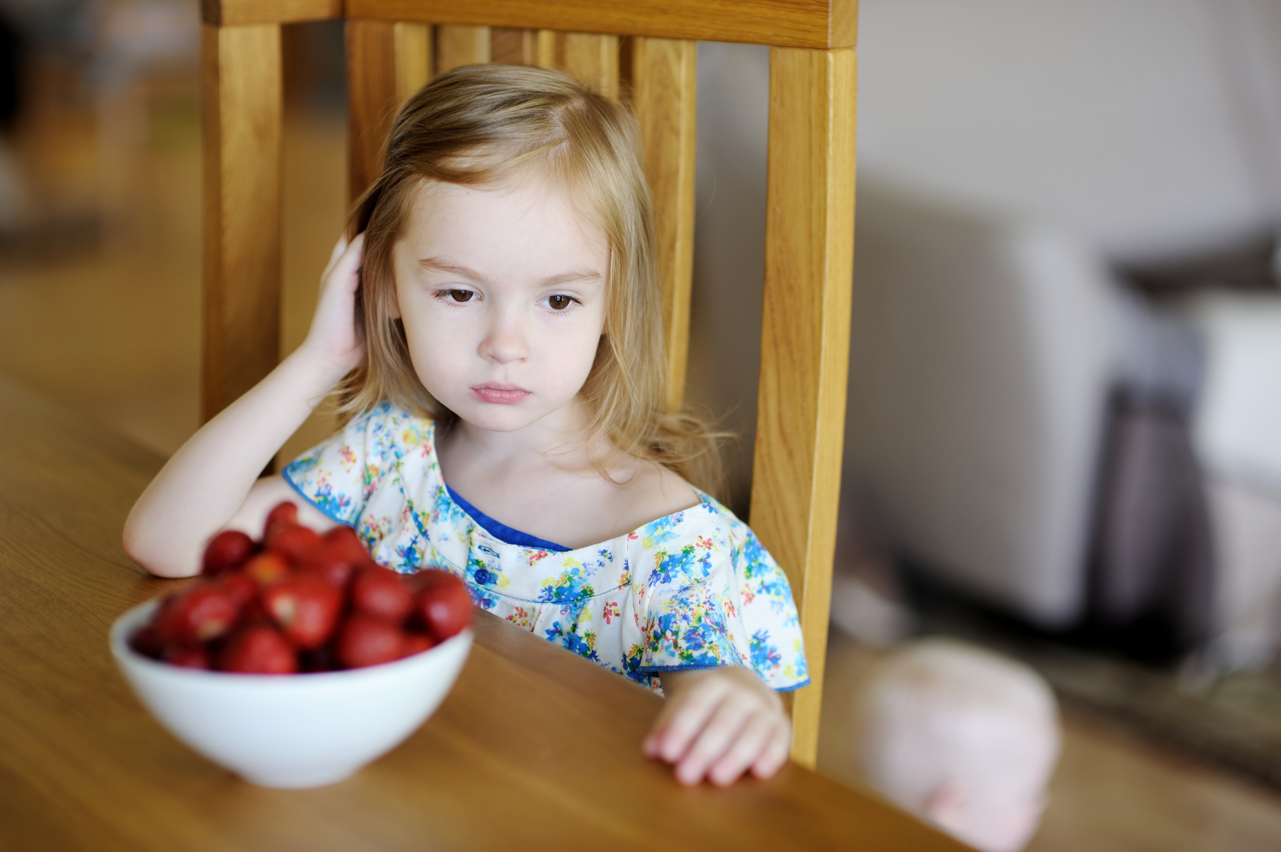 Little girl looking sad with a bowl of strawberries in front of her at the dining table | Source: Shutterstock