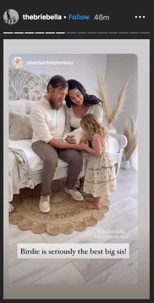 Photo of Brie and Bryan sitting on a white couch, holding Buddy on Brie's Instagram stories | Photo: Instagram /  thebriebella