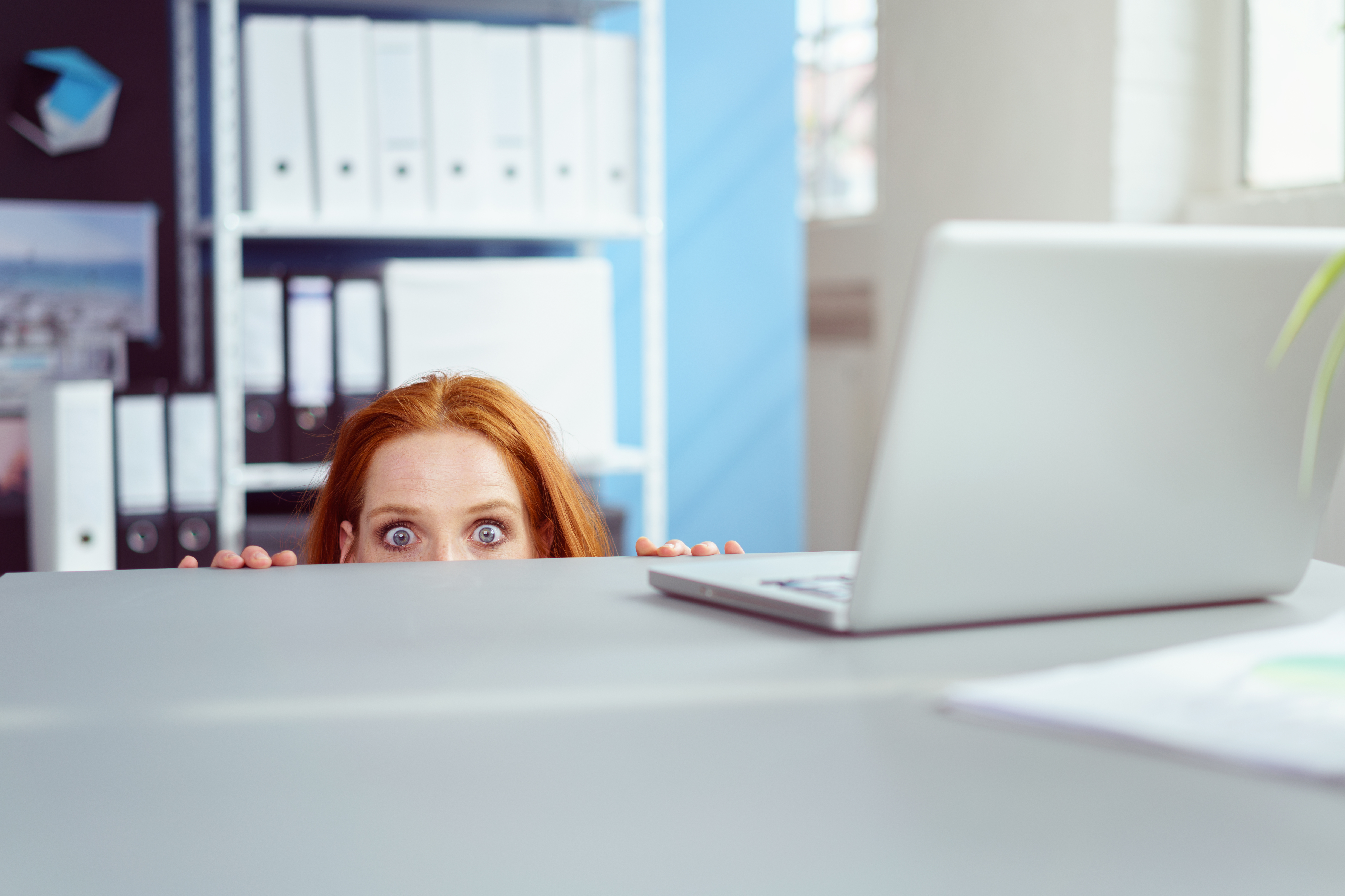 A woman hiding under a desk | Source: Shutterstock