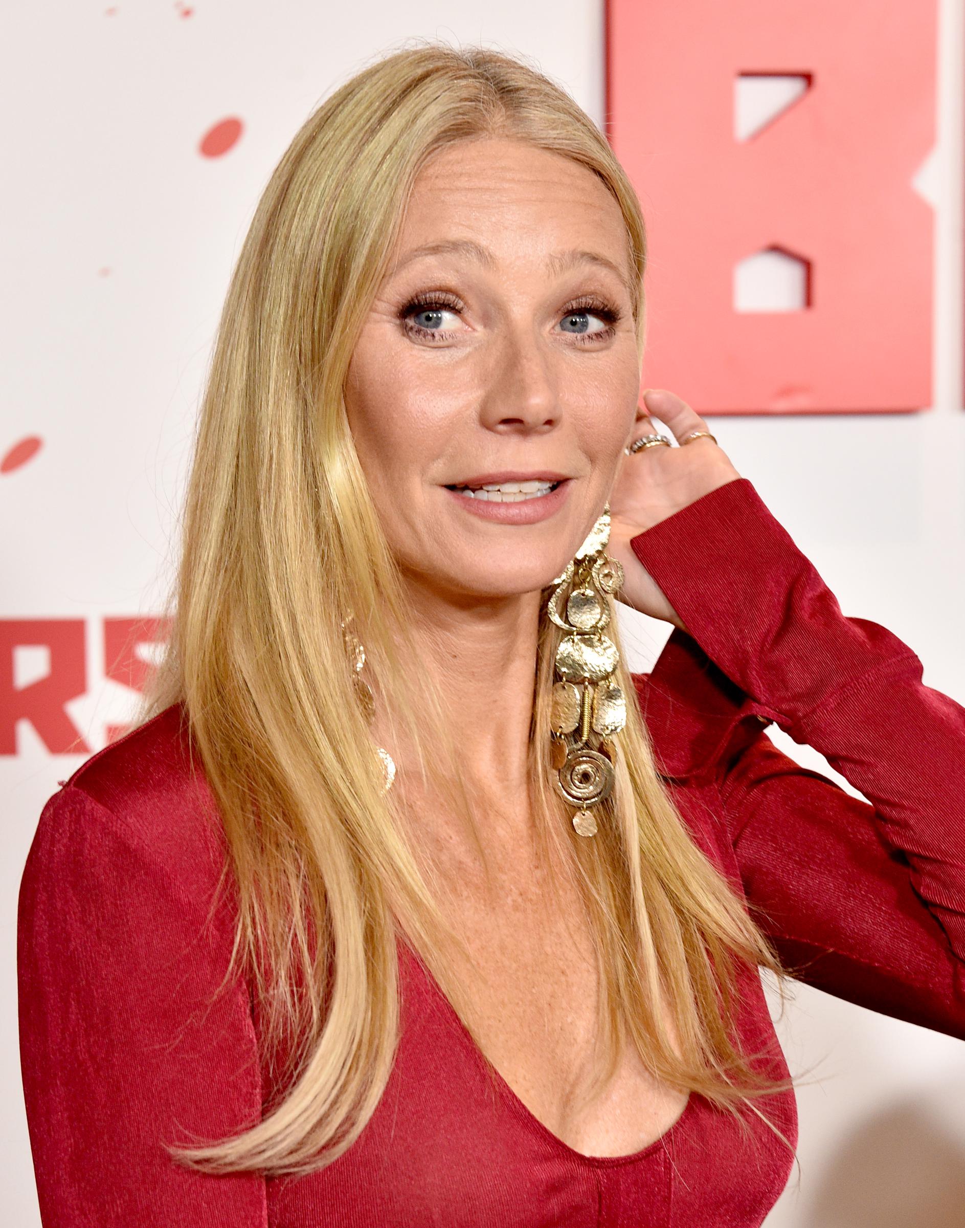 Gwyneth Paltrow is seen at a Los Angeles premiere on January 4, 2024, turning slightly as she lifts a hand to her hair, her expression animated and makeup softly defined.