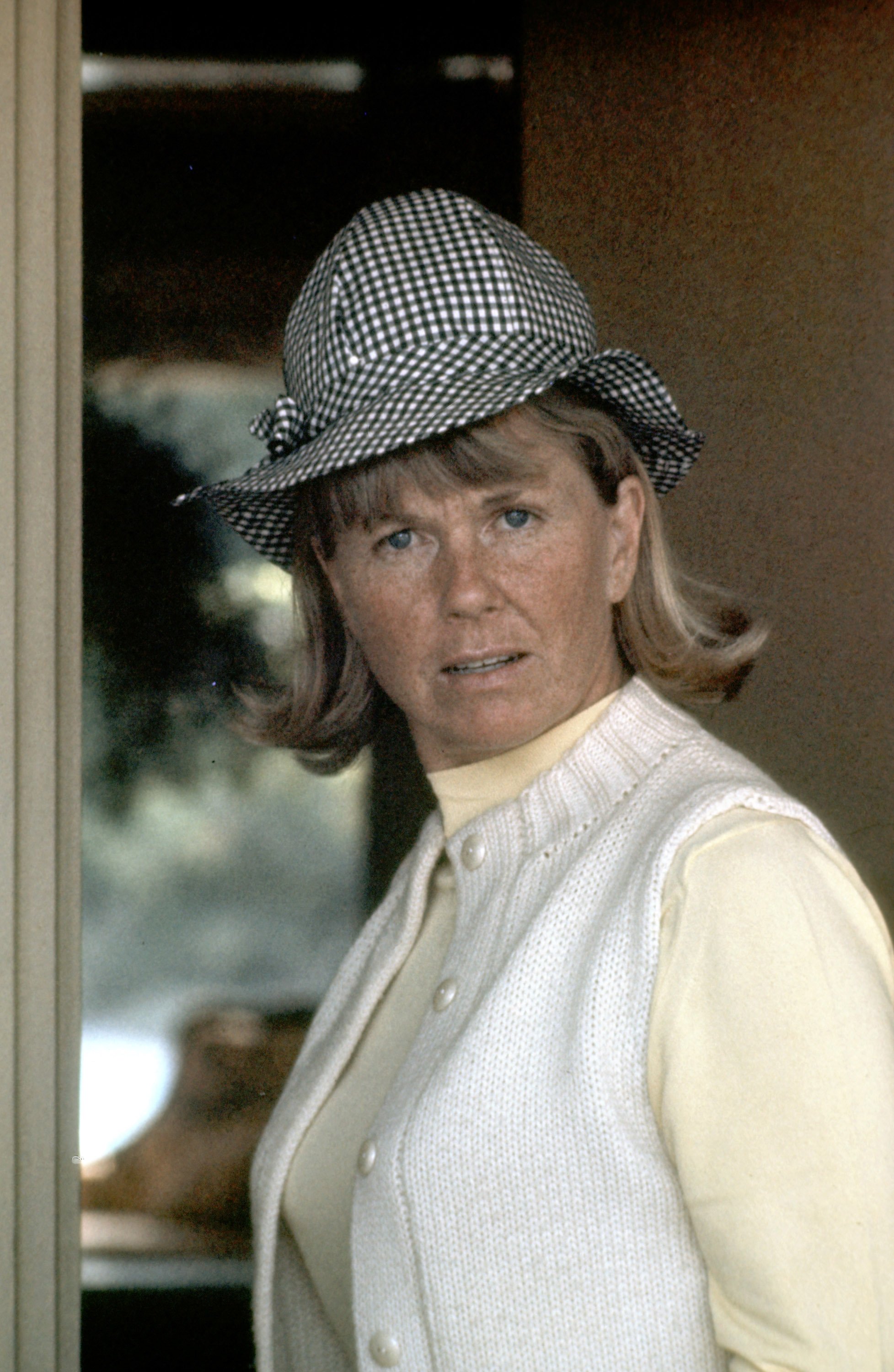Doris Day pictured showing a serious facial expression, wearing an off-white cardigan paired with a yellow sweater and a black and white hat. / Source: Getty Images