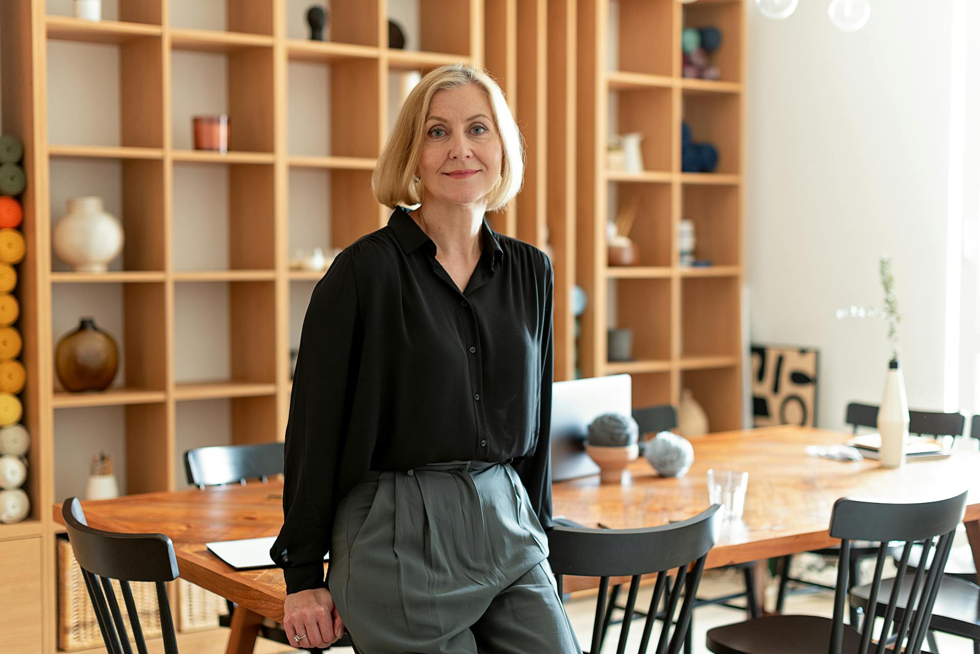 A smiling middle-aged woman leaning on a table in a formal setting | Source: Pexels