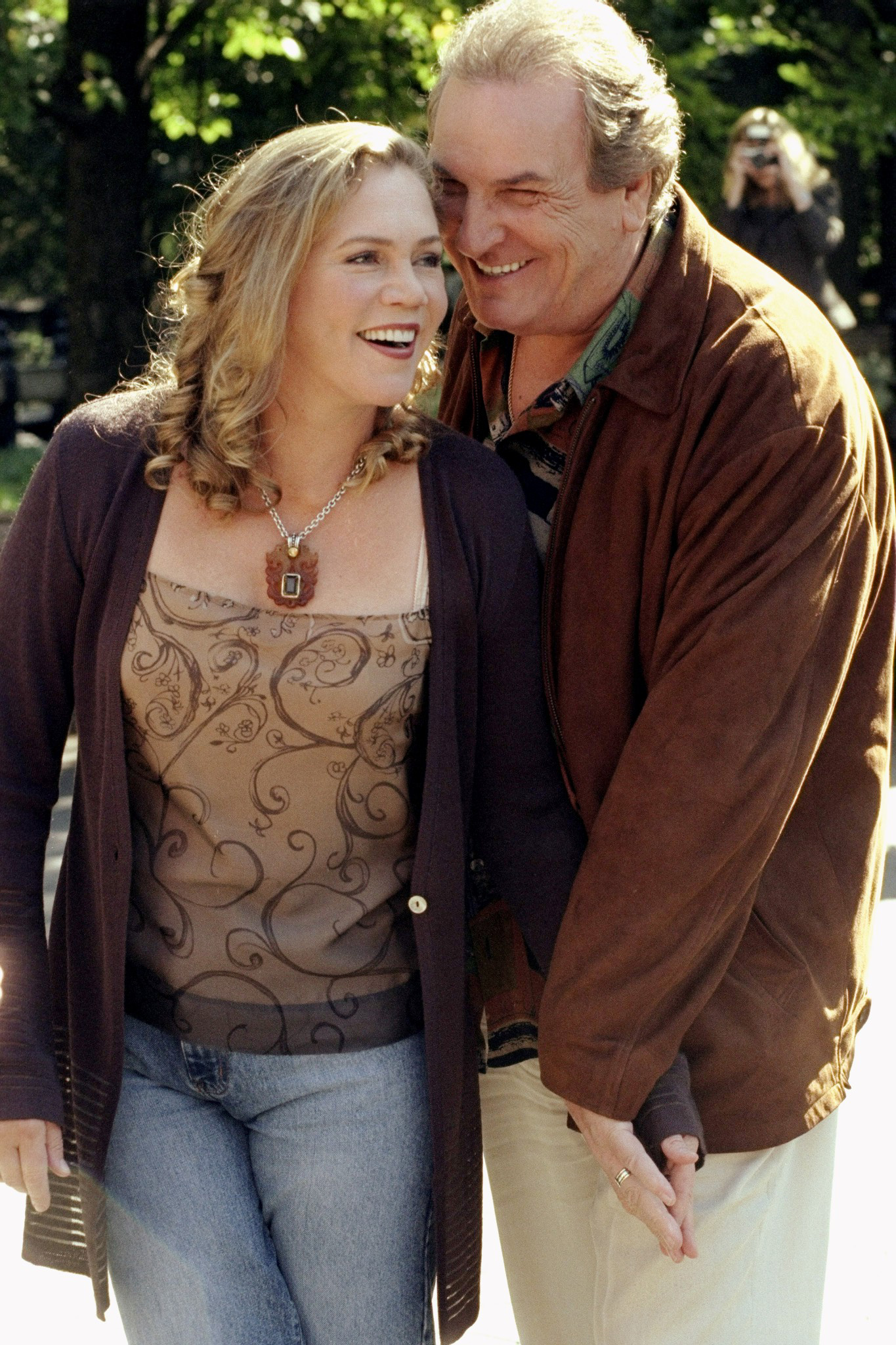 Kathleen Turner and Danny Aiello are filming a scene from "Prince of Central Park." The two are depicted as husband and wife, sharing a lighthearted, affectionate moment together in the park.