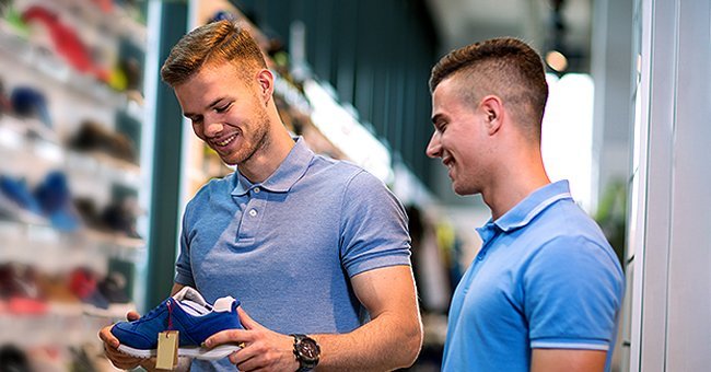 Two male friends at a store, smiling, and checking out sneakers | Photo: Shutterstock