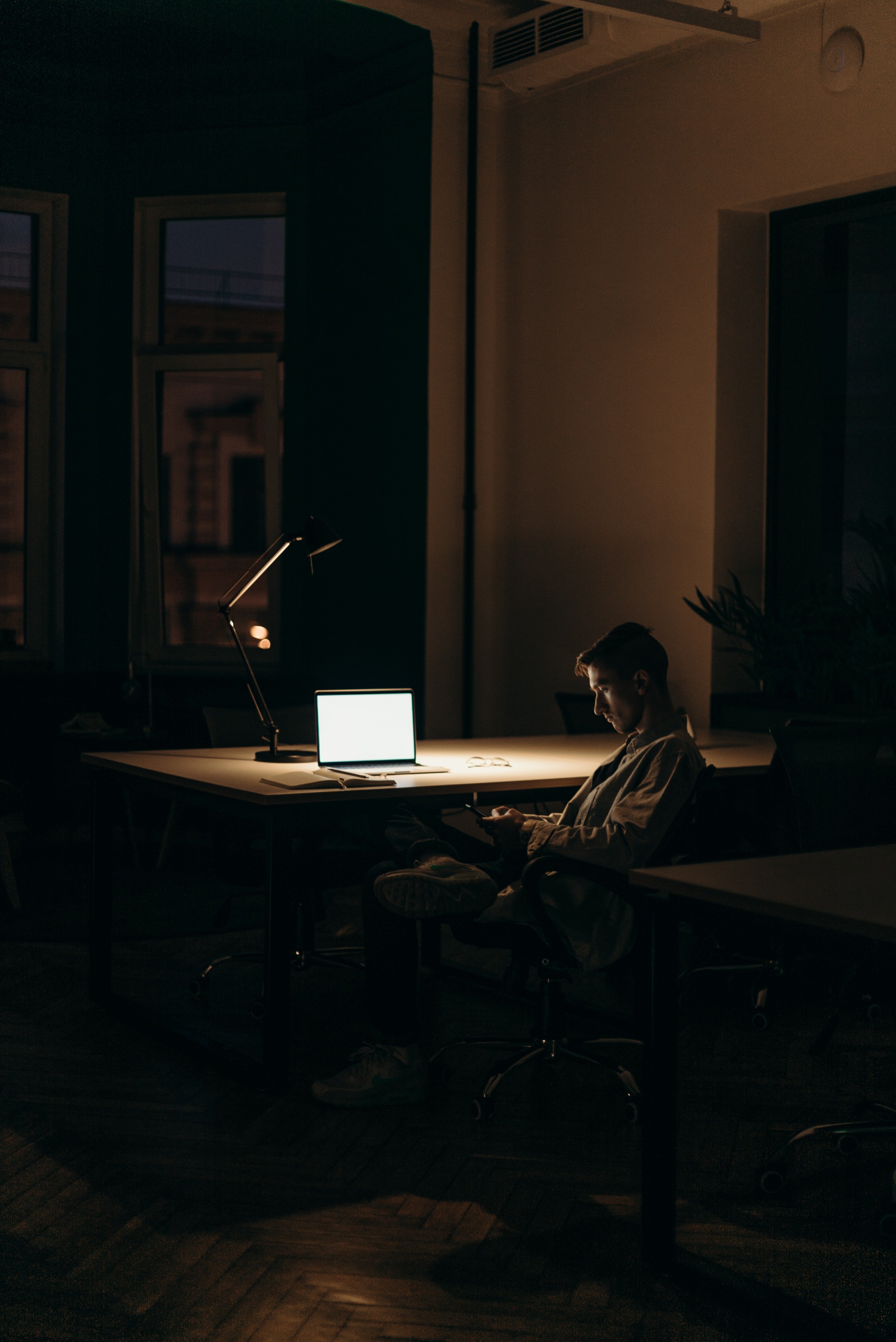 Man sitting behind a desk in a dark room with a laptop on. | Photo: Pexels