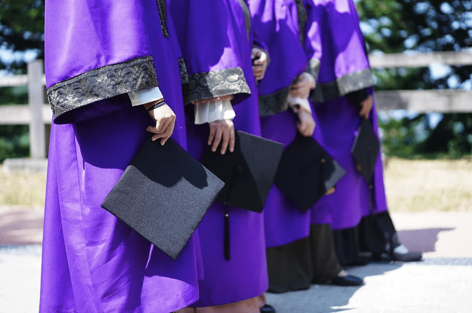 A photo of university graduates wearing purple robes hold their cap while posing together  | Photo: Pixabay