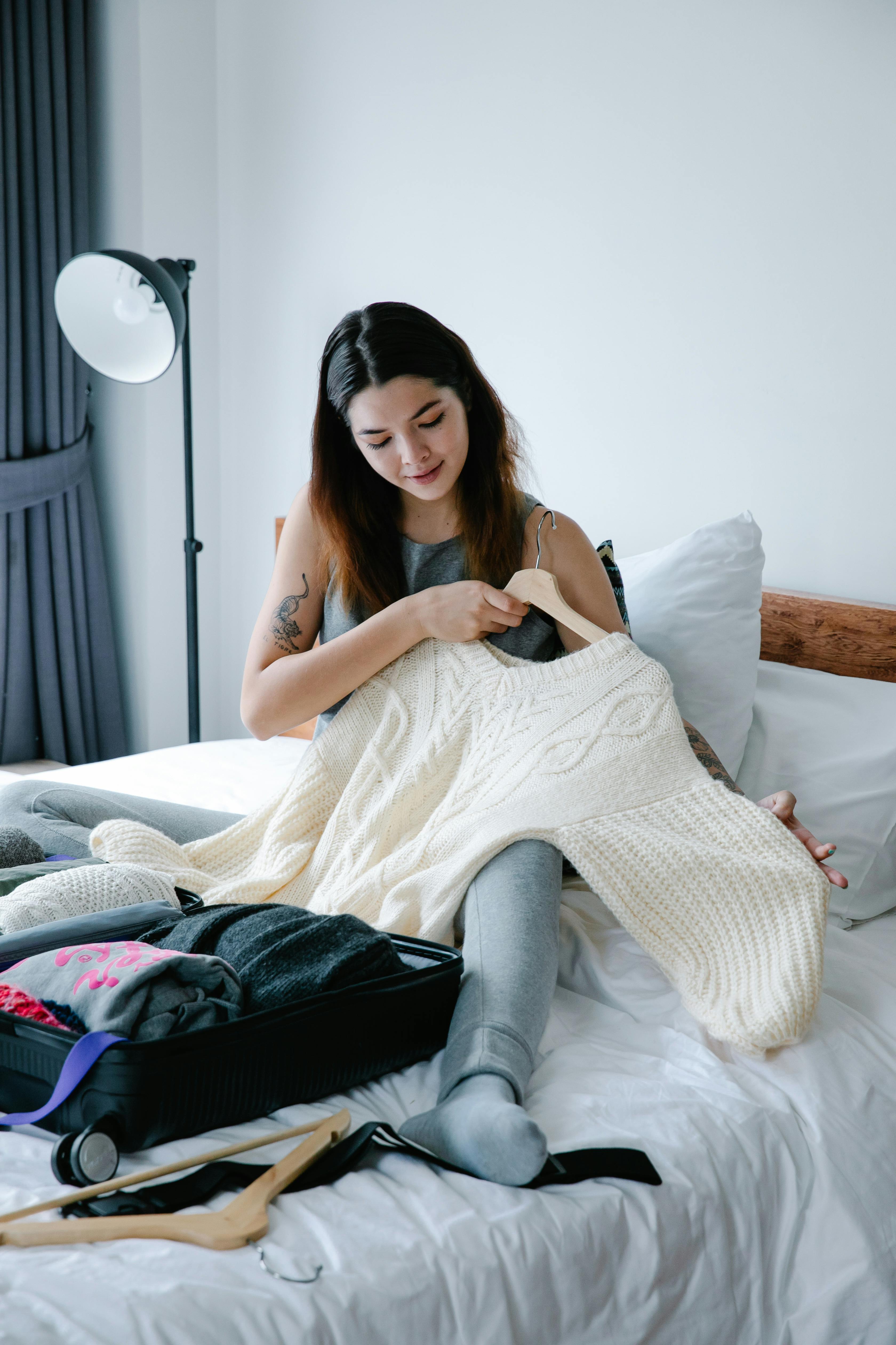 A woman sitting on the bed while holding a sweater | Source: Pexels