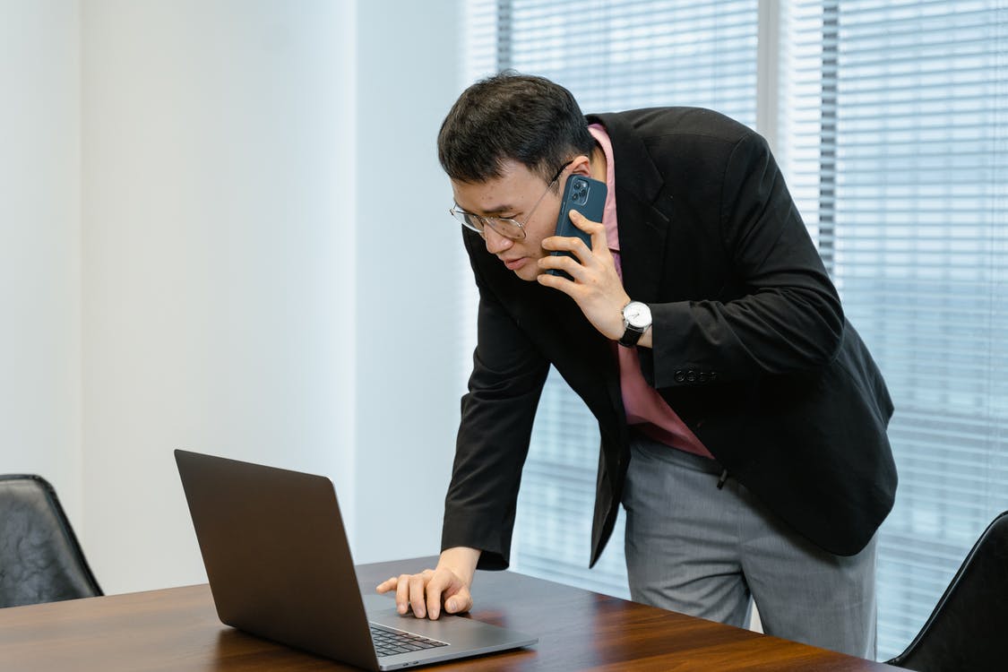 Hombre hablando por celular mientras revisa su computadora. | Foto: Pexels
