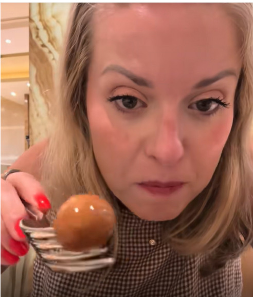 Amanda "Mandy" Karolkiewicz holds a small brown snack on a fork as she looks toward the camera while seated indoors during her trip to China. | Source: TikTok/mandykarolk