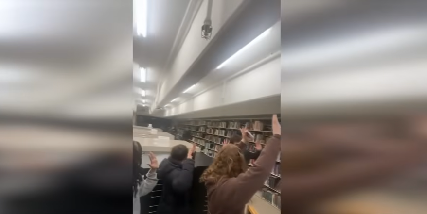 Students with their arms raised while authorities search the library, dated December 14, 2025 | Source: YouTube/WCVB Channel 5 Boston