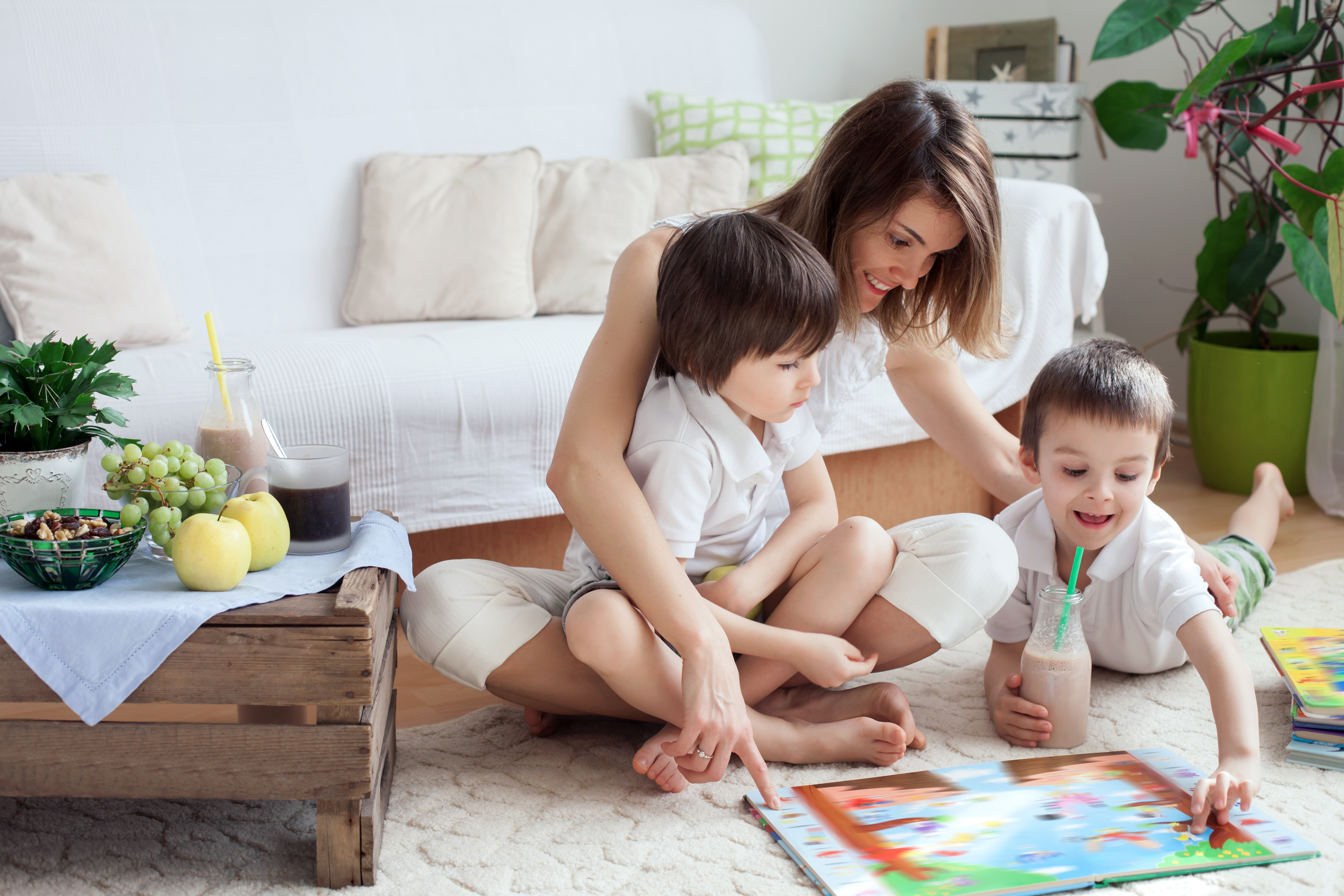 A woman on the floor reading a book with her two children | Source: Shutterstock