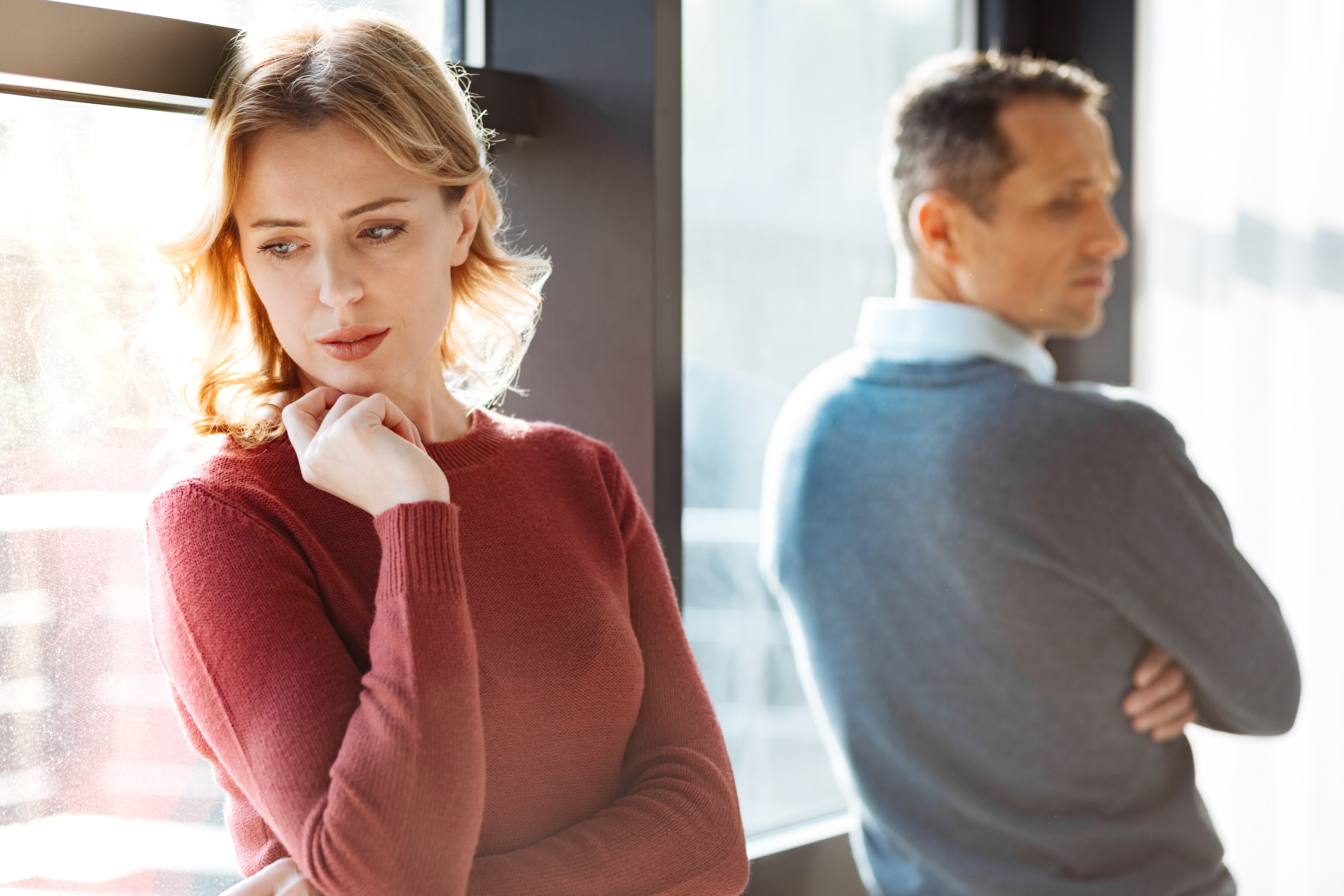 An unhappy woman standing close to the window after an argument with her husband | Source: Shutterstock