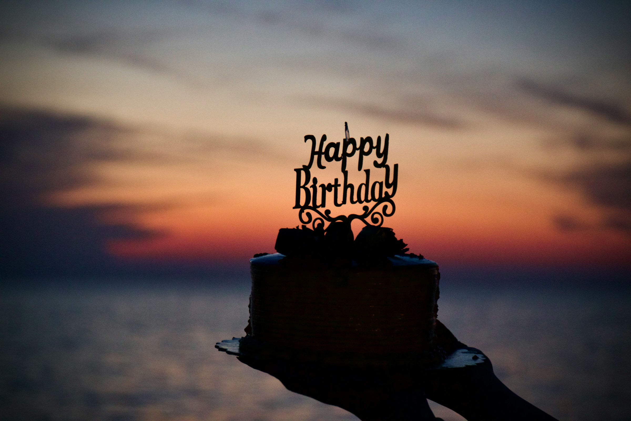 A person holding a birthday cake with sunset in the background | Source: Unsplash