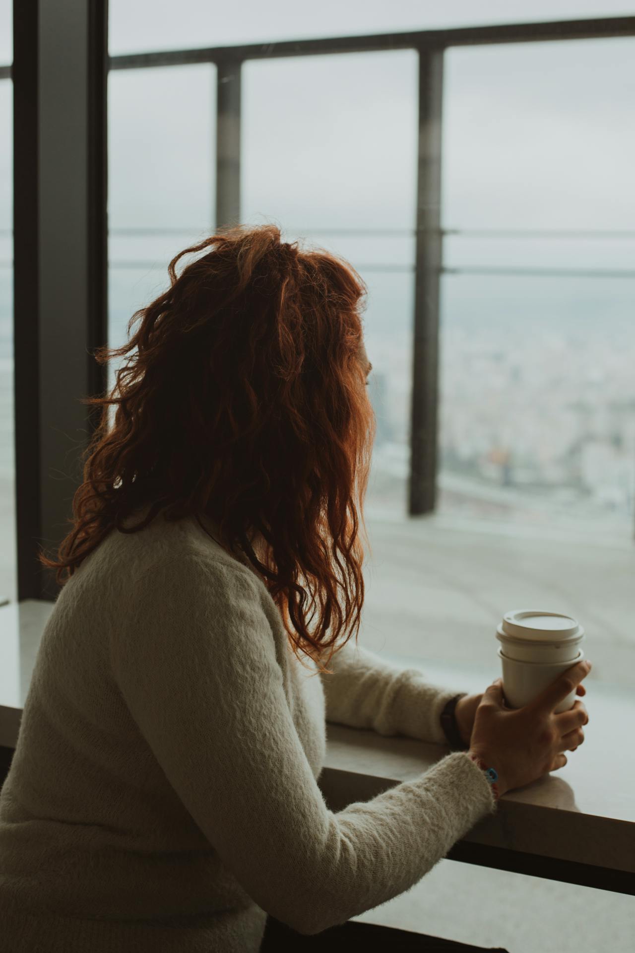 A woman sitting with a coffee cup in front of a glass window | Source: Pexels