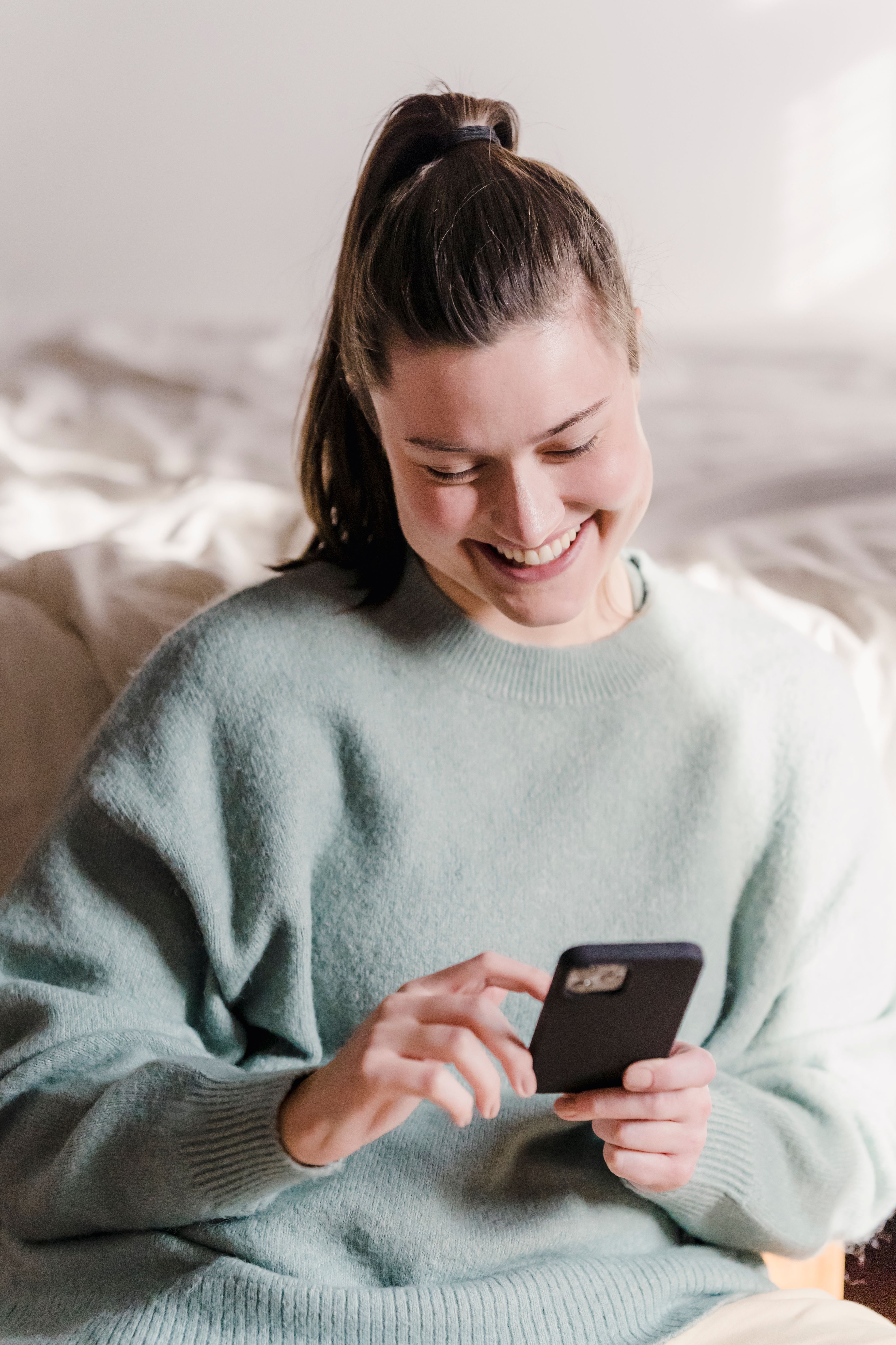 A woman smiling as she looks at her smartphone | Source: Pexels