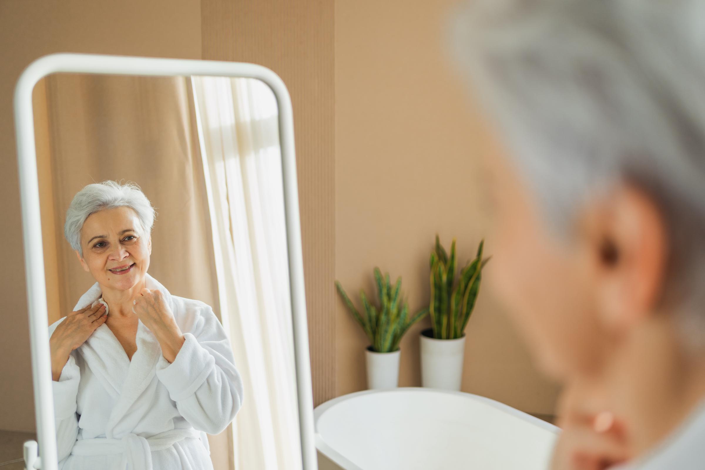 Woman wearing a bathrobe and admiring herself in the mirror | Source: Shutterstock