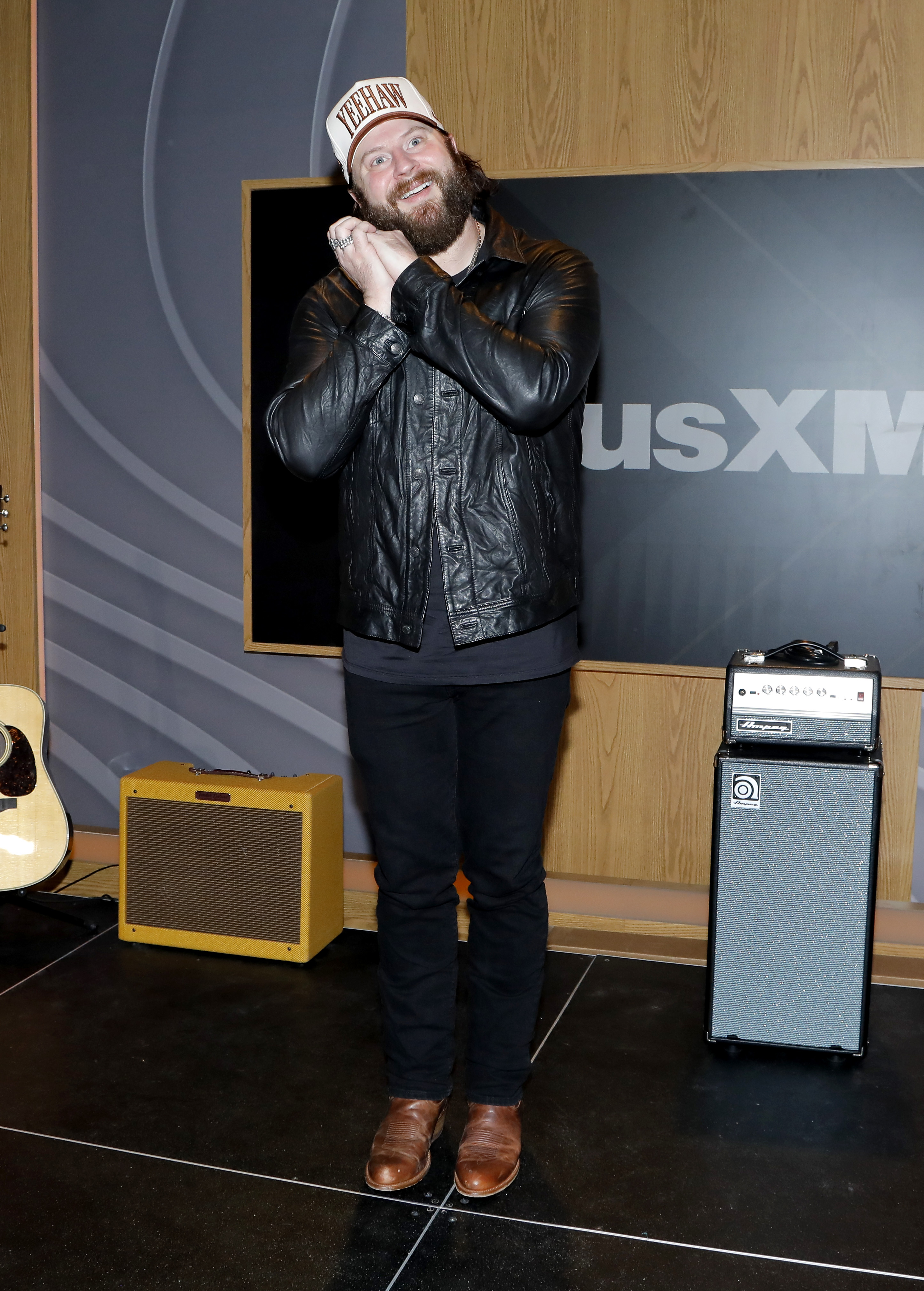 Nate Smith shows his playful side during a SiriusXM studio visit, tilting his head onto his clasped hands and flashing a wide-eyed smile for the camera.