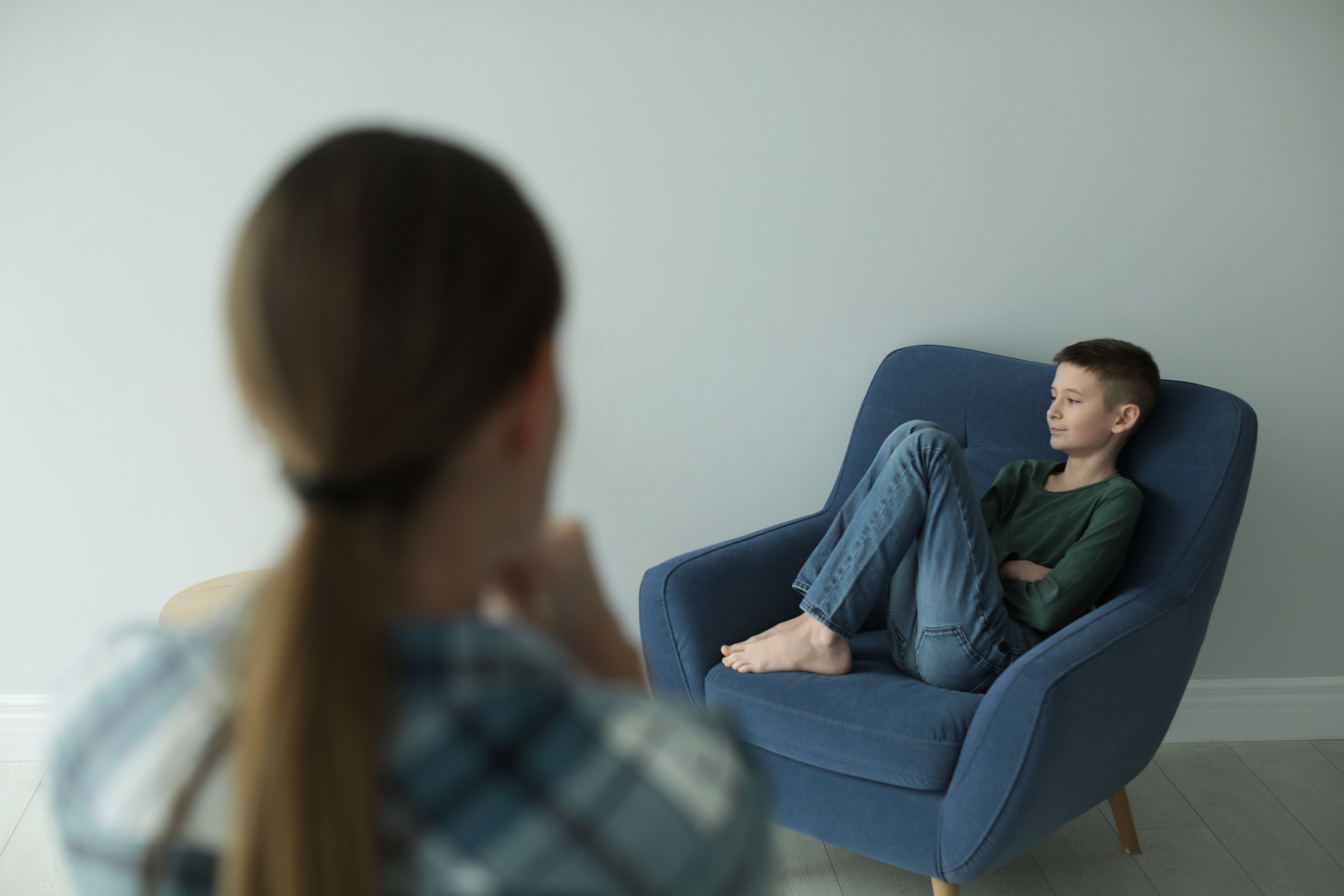 A young boy sitting on a chair as a woman looks on | Source: Shutterstock