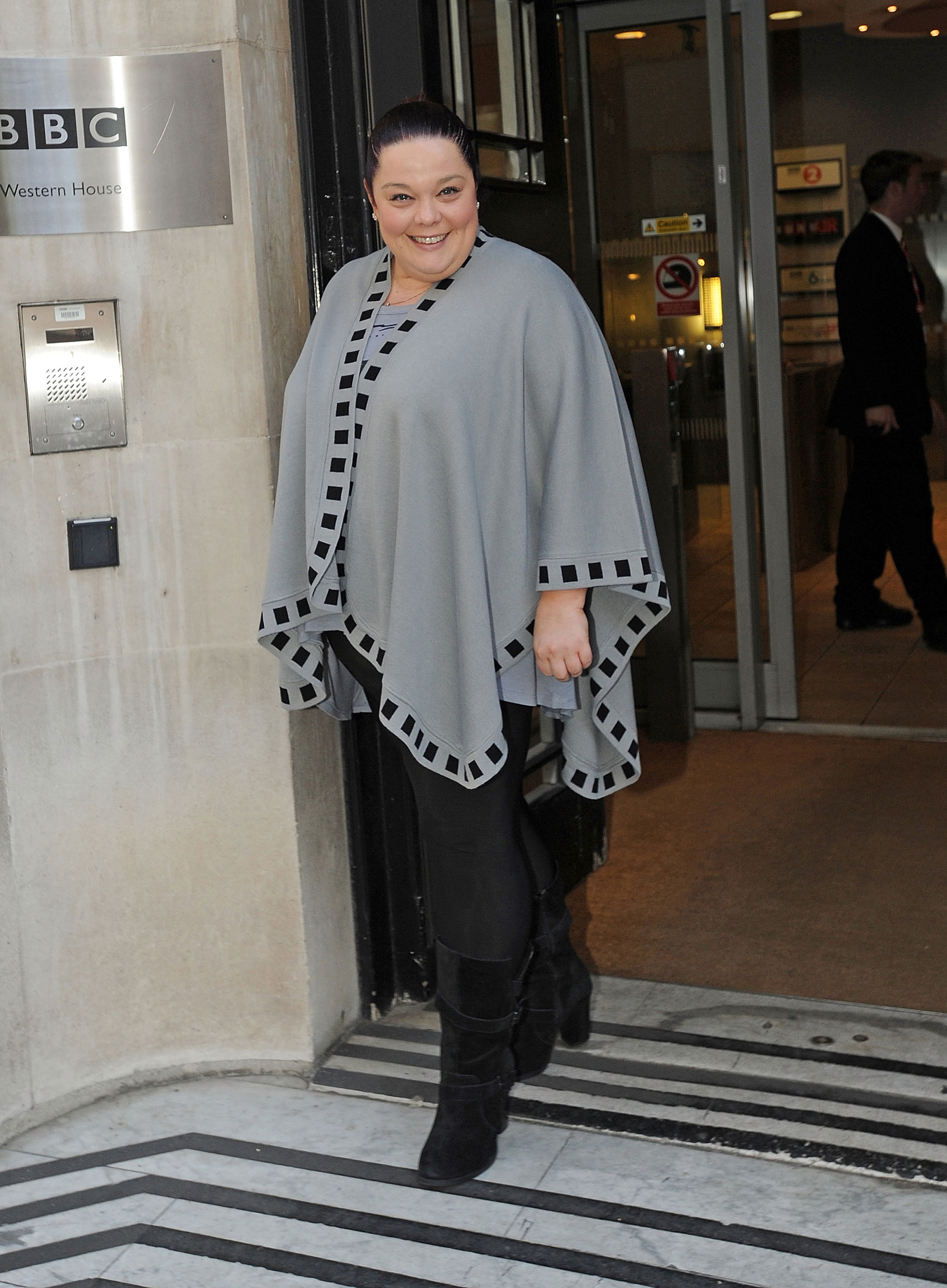 Radiant and ready for the spotlight! Lisa Riley beams outside BBC Radio 1 studios on 2 November 2012, wrapped in a chic grey cape and sleek all-black look as she commands attention at the iconic London landmark.