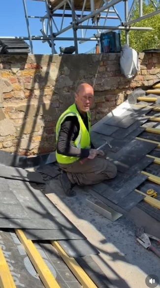 In a post dated 22 April 2026, John Hendy is captured kneeling on a sloped rooftop, tools in hand as he carefully works on laying tiles. Dressed in a hi-vis vest and practical workwear, the image highlights the physical, detail-oriented nature of his day-to-day job, a stark contrast to his former life on stage. | Source: Instagram/johnhendyeast17_official