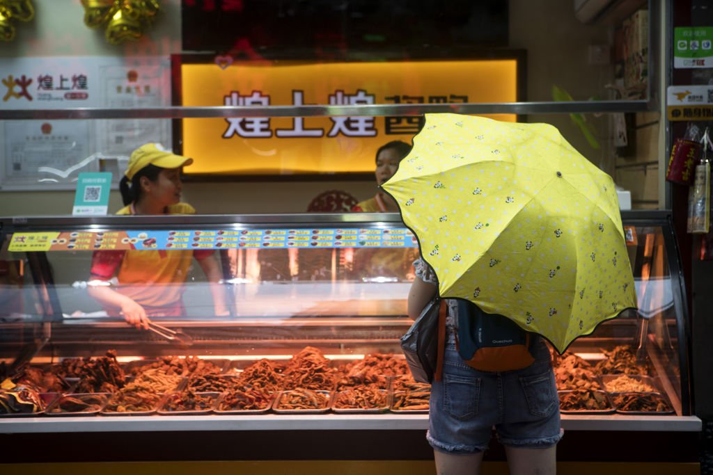 Un cliente con un paraguas se encuentra en una tienda de alimentos mientras cae la lluvia en Shenzhen, China. | Foto: Giulia Marchi a través de Getty Images