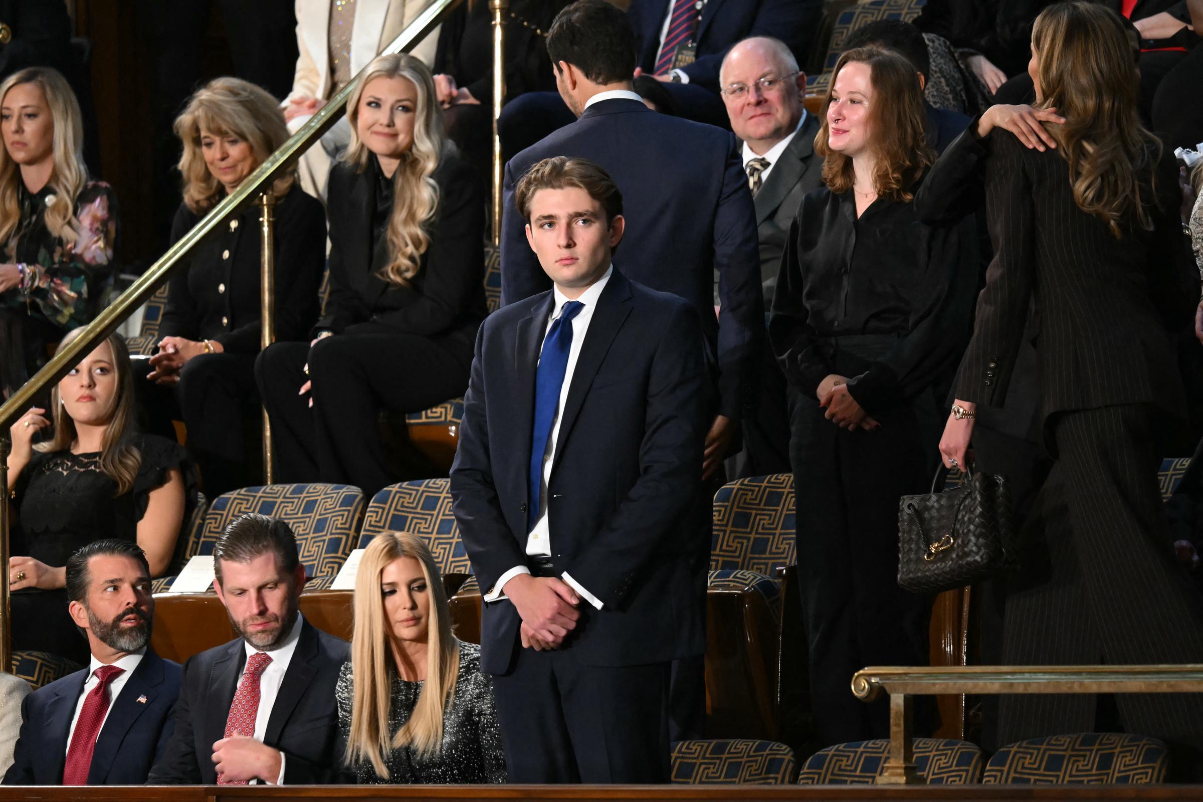 Barron Trump stands quietly in the House Chamber ahead of the State of the Union address in Washington, DC. Dressed in a navy suit and blue tie, he waits as guests settle into their seats around him. Members of the Trump family sit nearby as the chamber prepares for the President’s arrival.