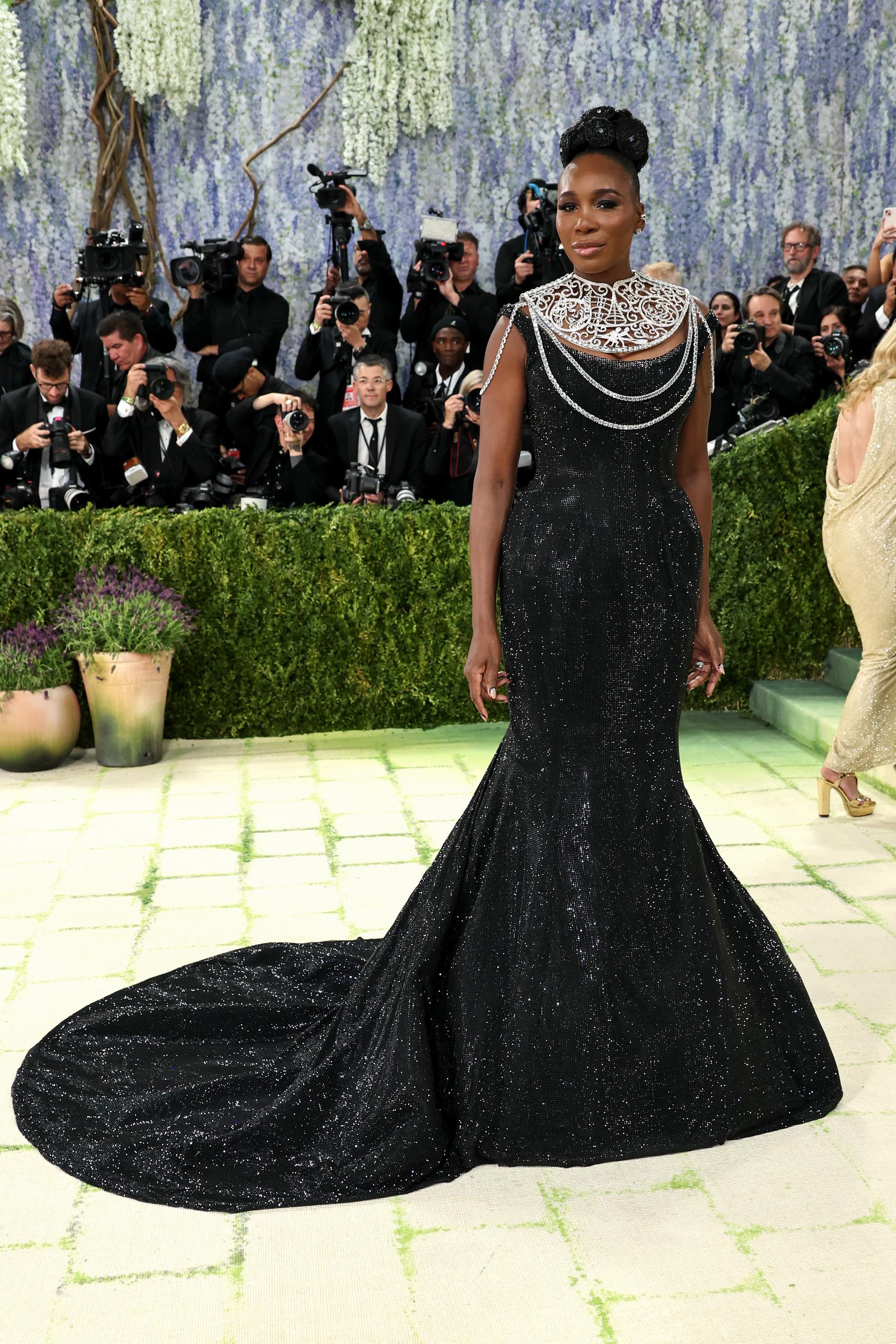 Venus Williams commands the 2026 Met Gala carpet in a sparkling black mermaid gown with a long train, finished with an ornate silver collar and layered chain details.