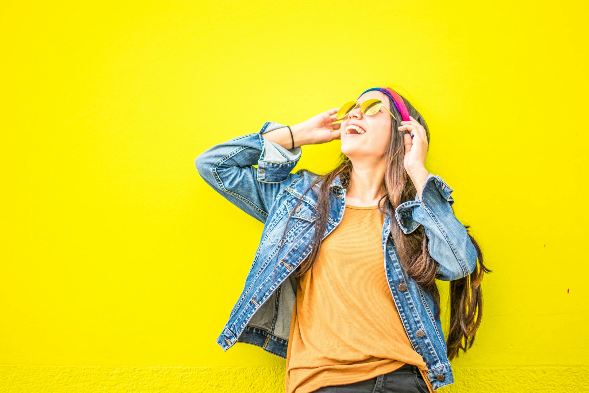 A smiling woman looking up while standing against a yellow wall | Source: Pexels