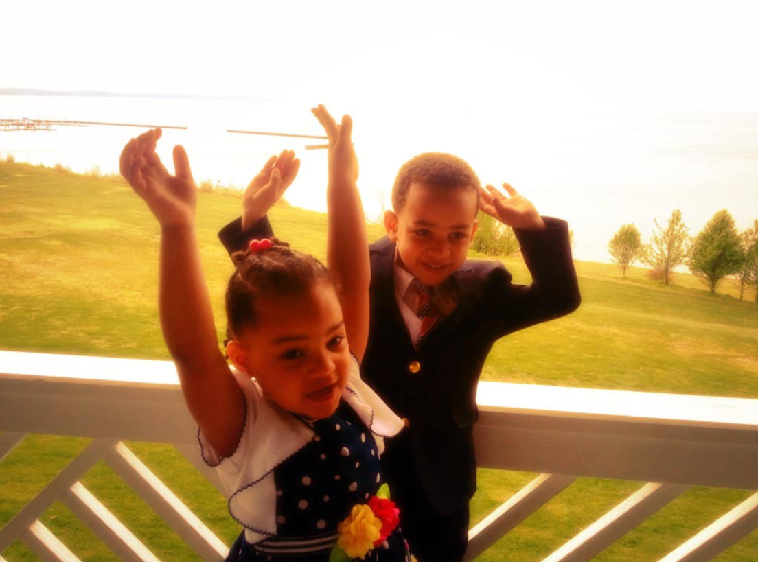 Cameron and Carys Fairfax raise their arms while posing outdoors in a childhood photo | Source: Facebook/justin.fairfax.2025