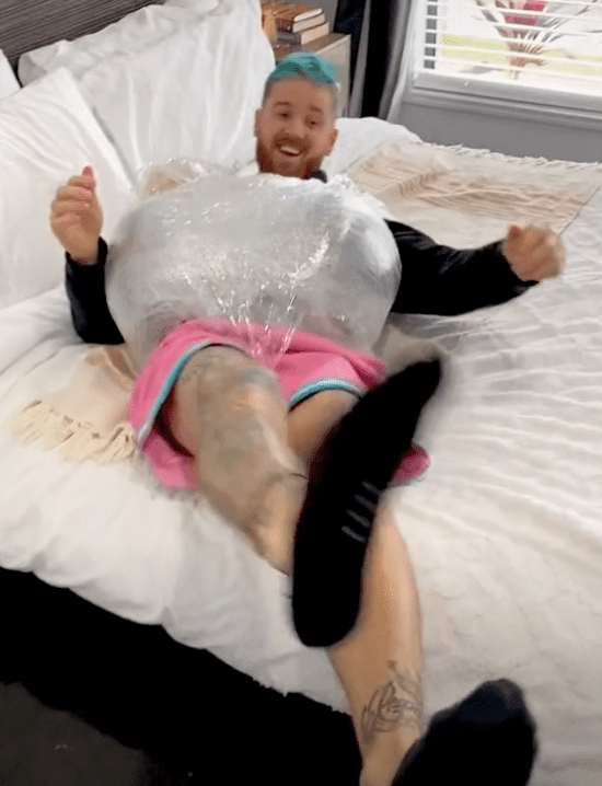 A man tries to get out of bed with two watermelons strapped on his belly to imitate what women experience when they are expecting twins | Photo: TikTok/MaitlandHanley