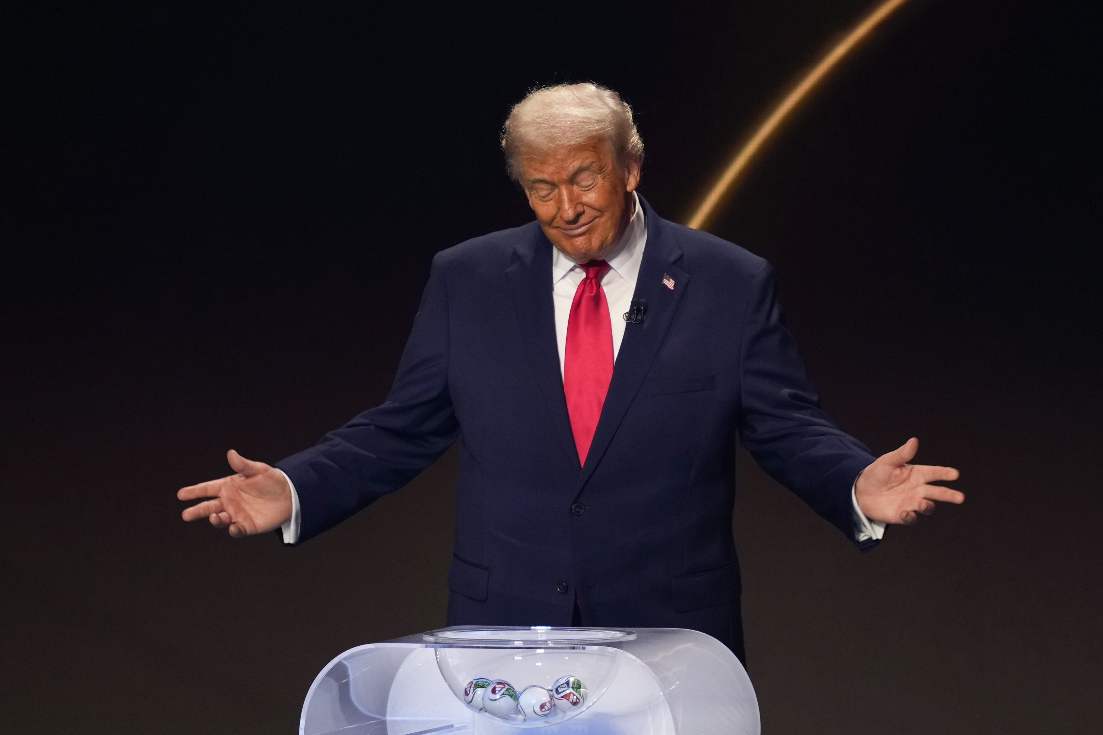 Donald Trump shrugs and smiles onstage during the FIFA World Cup 2026 Official Draw in Washington, D.C., on December 5, 2025. | Source: Getty Images