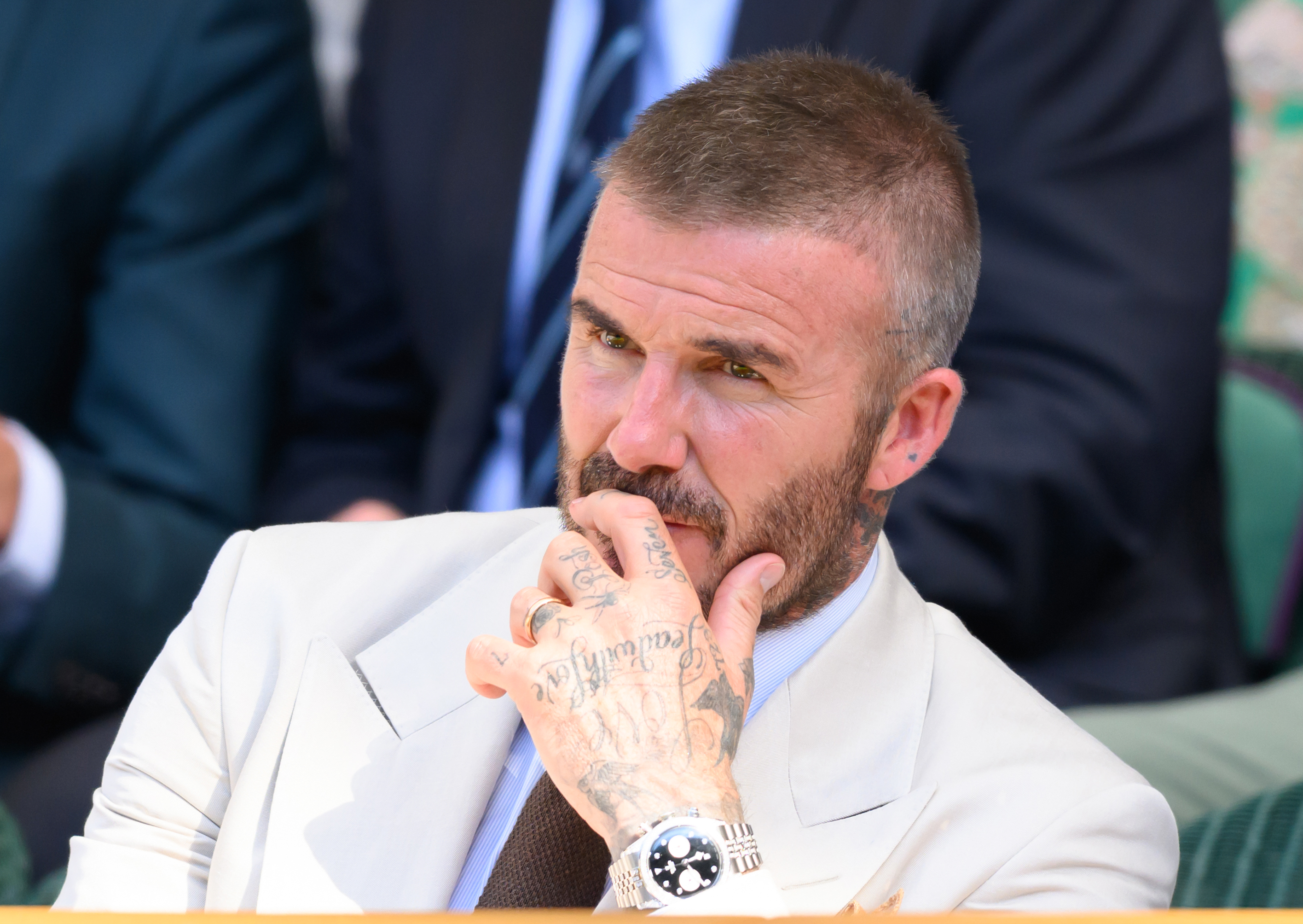 David Beckham is seen at day one of the Wimbledon Championships on June 30, 2025, at the All England Club. He rests his chin on his tattooed fingers as he watches the match, his wrist still wrapped in a bandage.